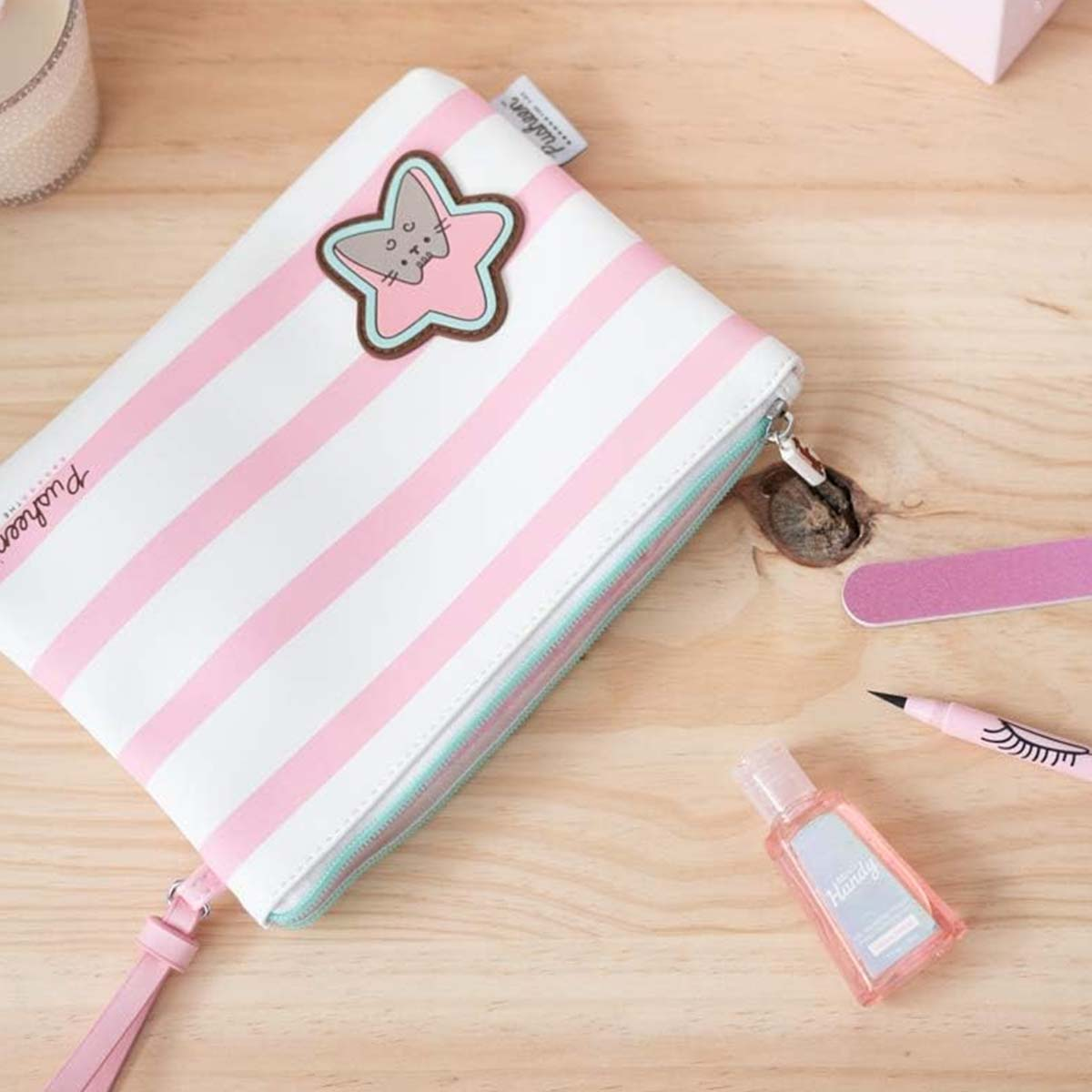 Una trousse a righe rosa e bianche con una toppa a forma di stella di Pusheen. Lime per unghie e disinfettante per le mani accanto.