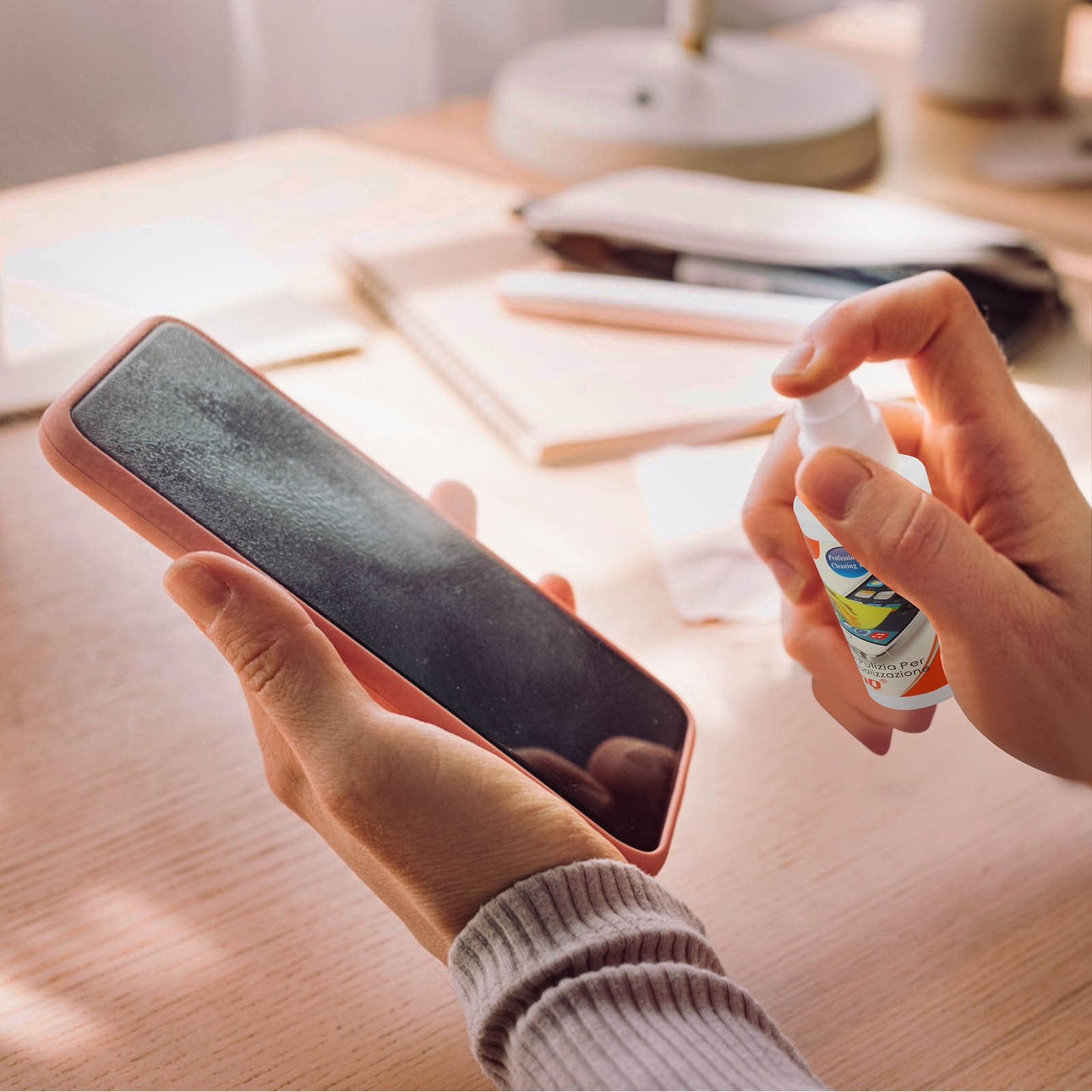 Una mano spruzza un detergente per schermo su uno smartphone in una custodia.