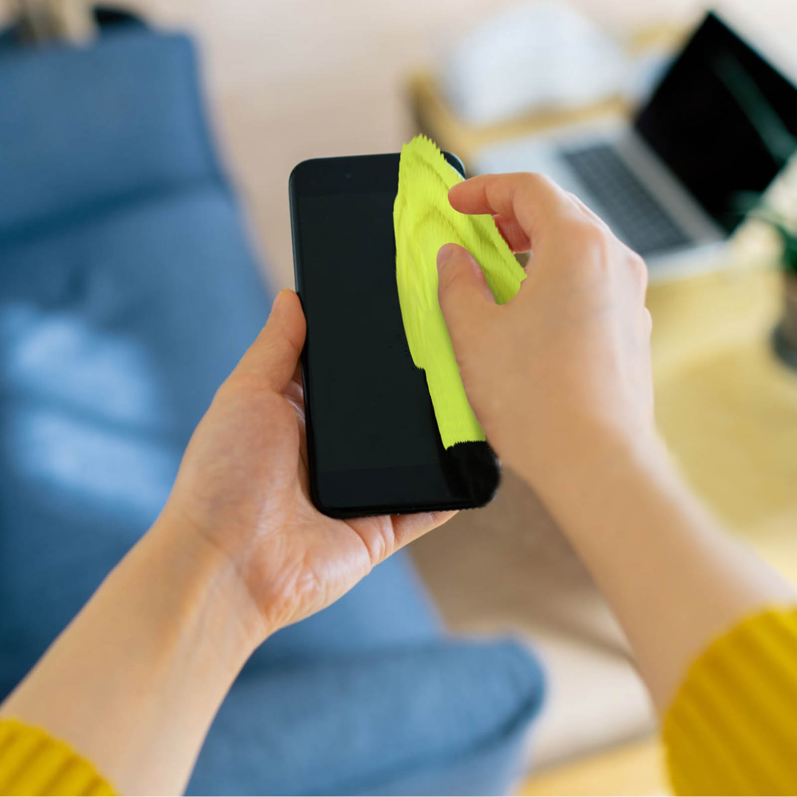 Mani che puliscono uno smartphone con un panno giallo.