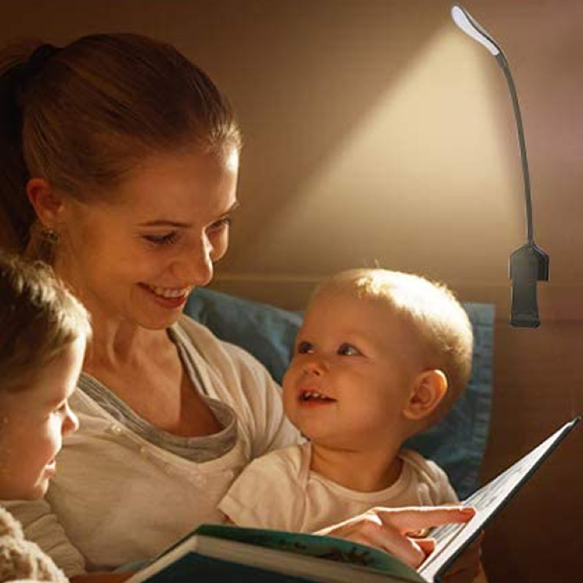 Eine Frau liest zwei Kindern ein Buch vor, beleuchtet von einer Klemmlampe.