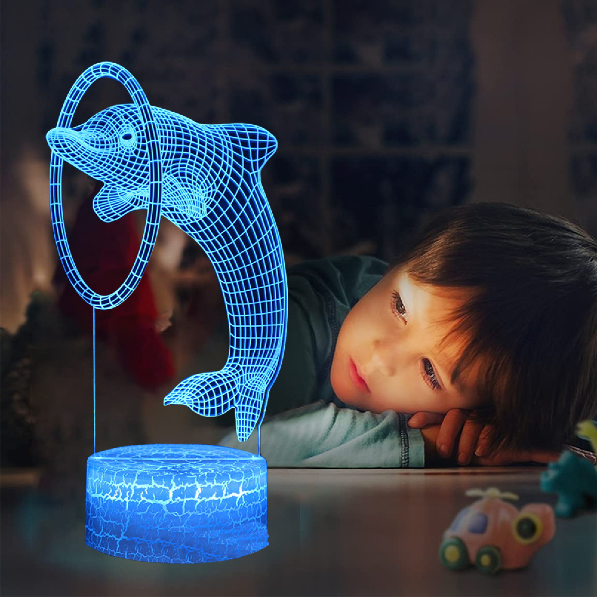 Ein Junge schaut auf eine blaue Delfinlampe, die auf einem Tisch steht.