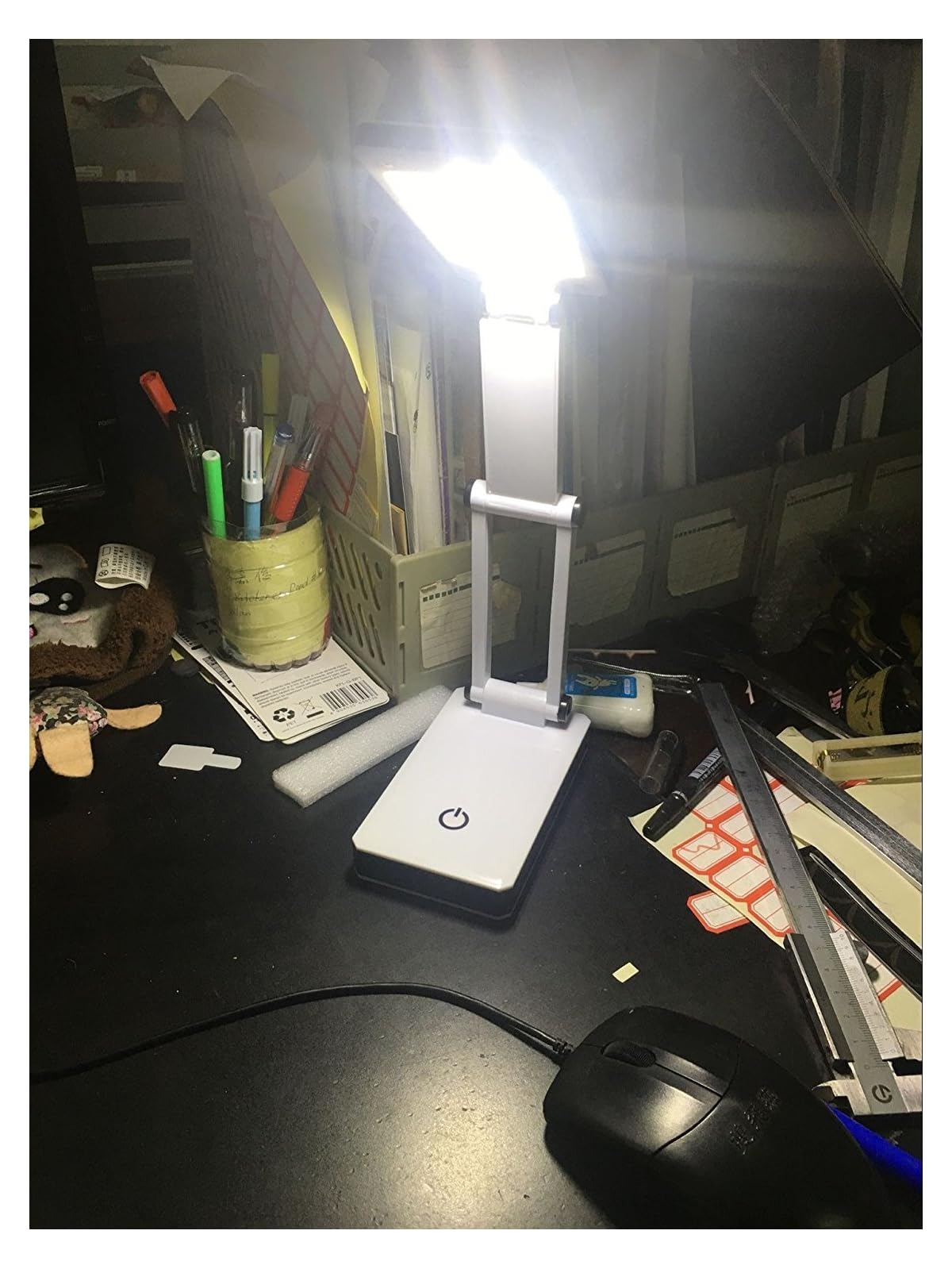 Eine weiße LED-Schreibtischlampe mit einem Powesymbol steht auf einem dunklen Schreibtisch mit einer Computermaus.