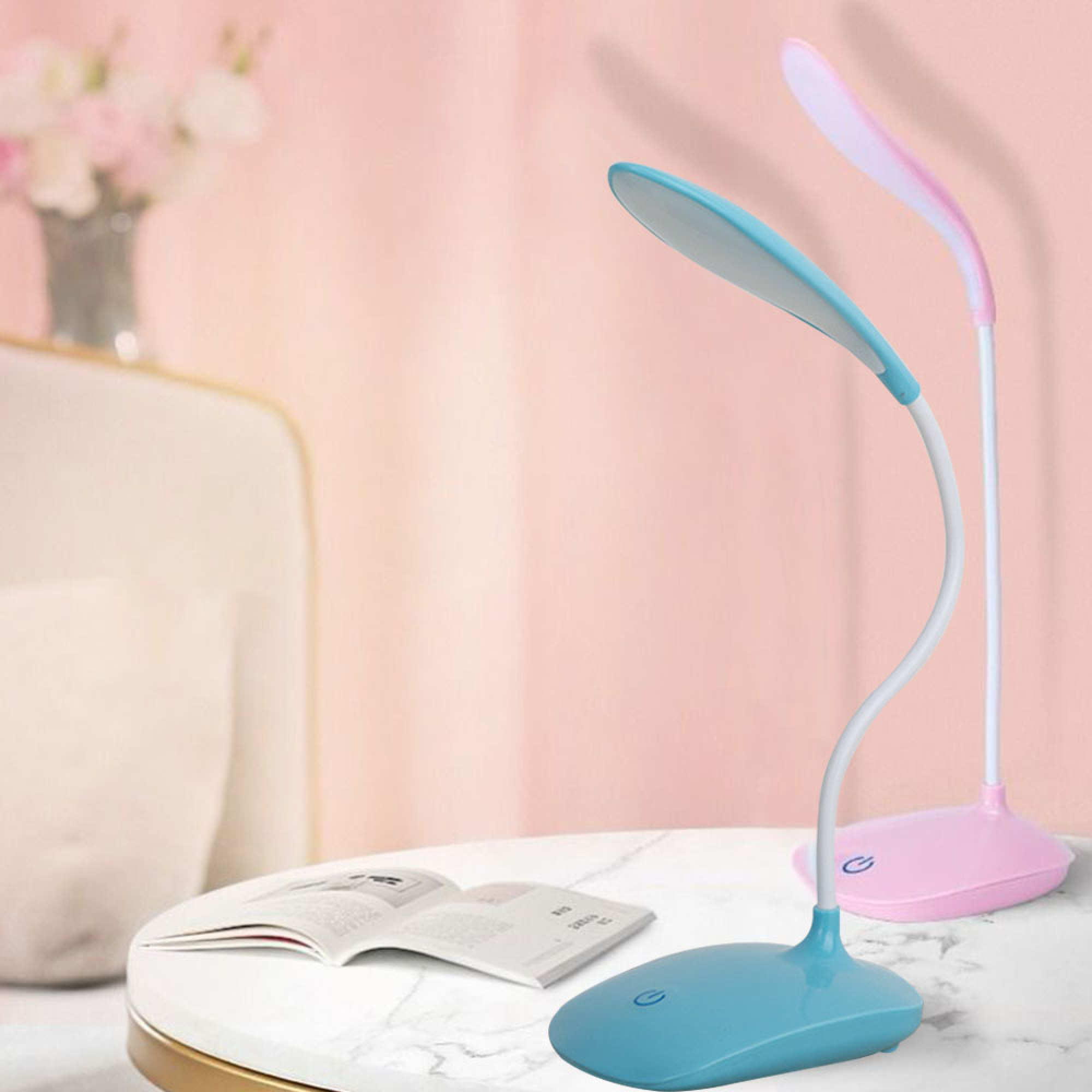 Zwei Nachttischlampen, eine blau, eine rosa, auf einem Tisch mit einem offenen Buch.