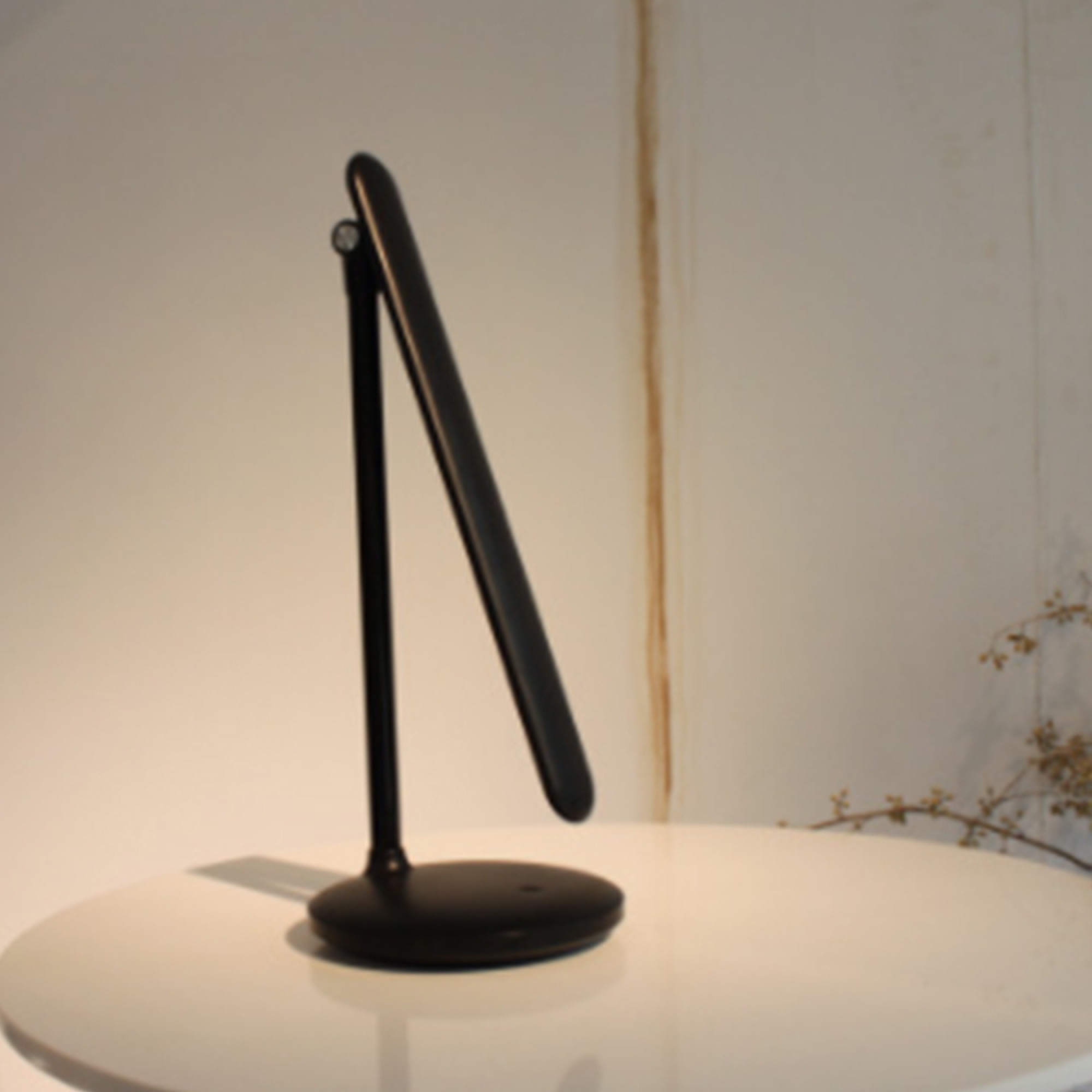 Eine schwarze moderne Schreibtischlampe mit verstellbarem Arm steht auf einem weißen Tisch.