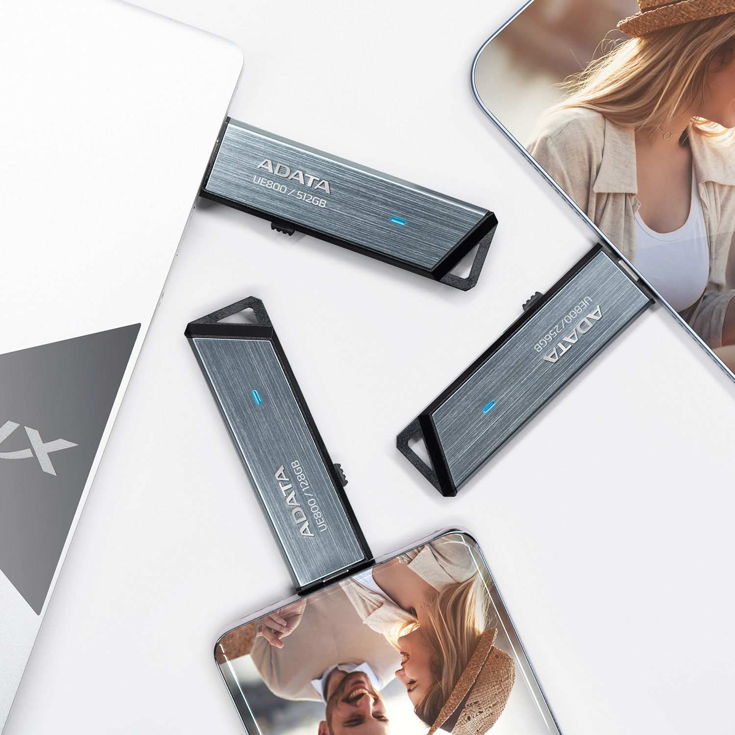 Drei USB-Sticks liegen neben einem Laptop und auf zwei Fotos.