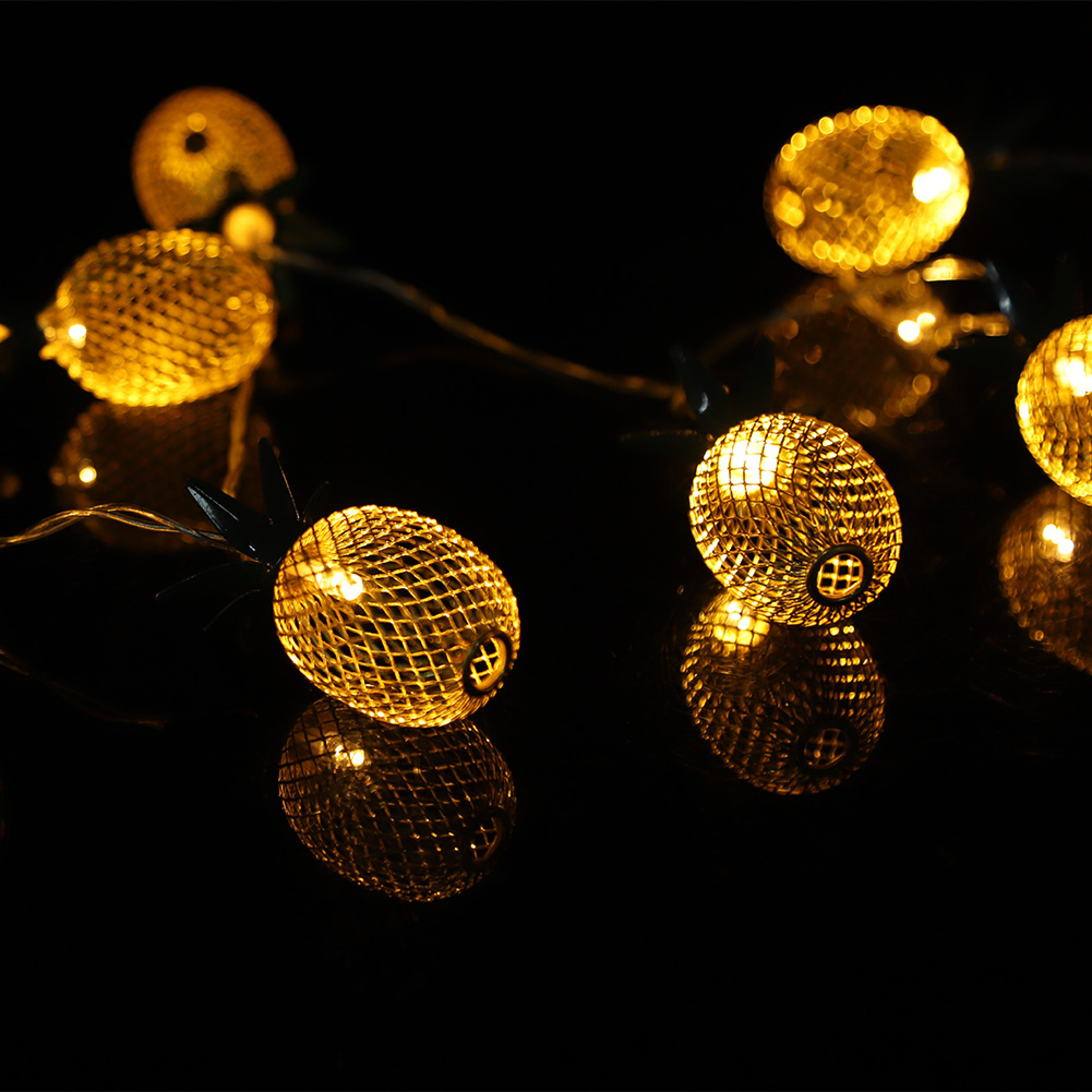 Goldene ananasförmige Lichterketten leuchten warm vor dunklem Hintergrund.