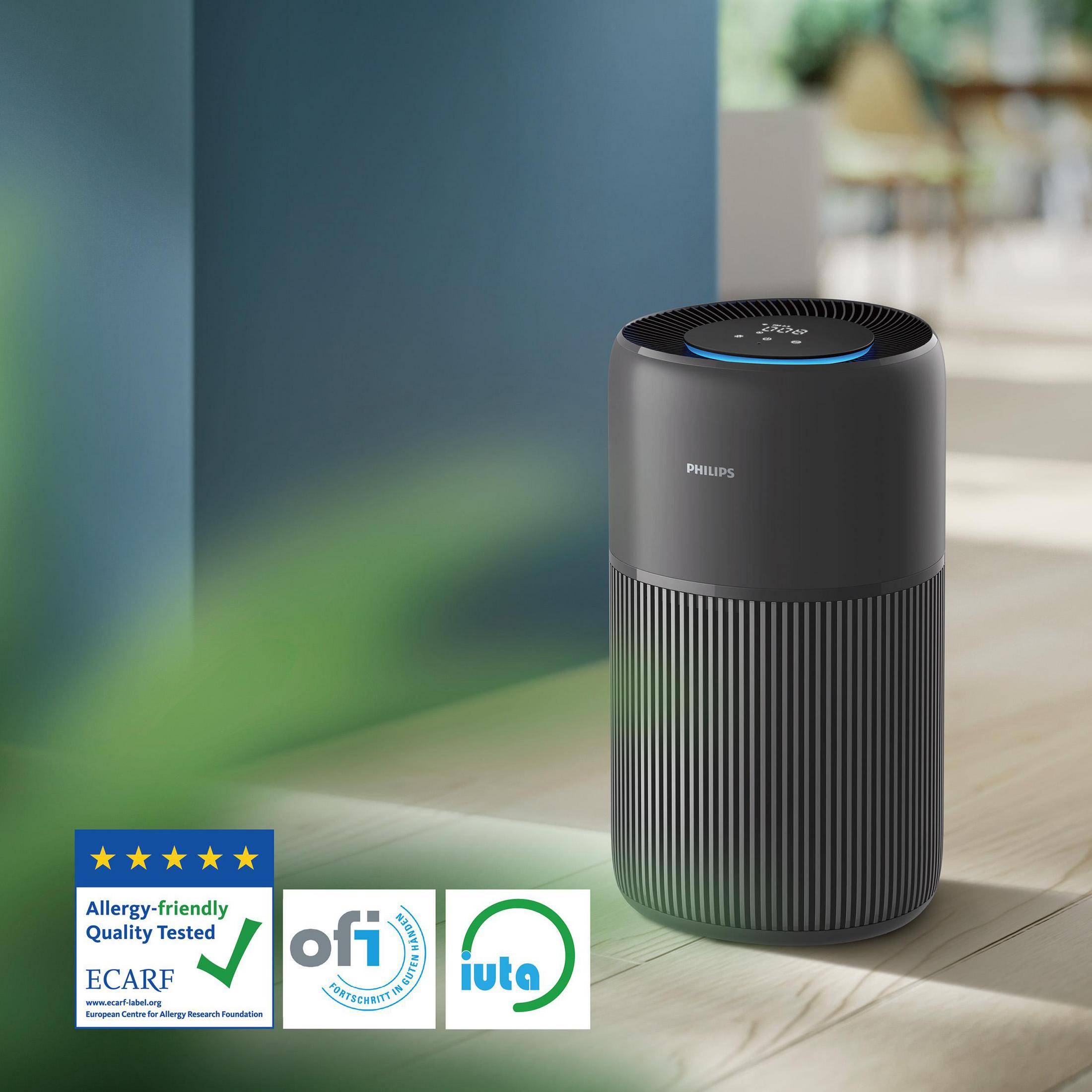 Ein schwarzer Philips Luftreiniger steht auf einem Holzboden, mit Zertifikaten daneben.