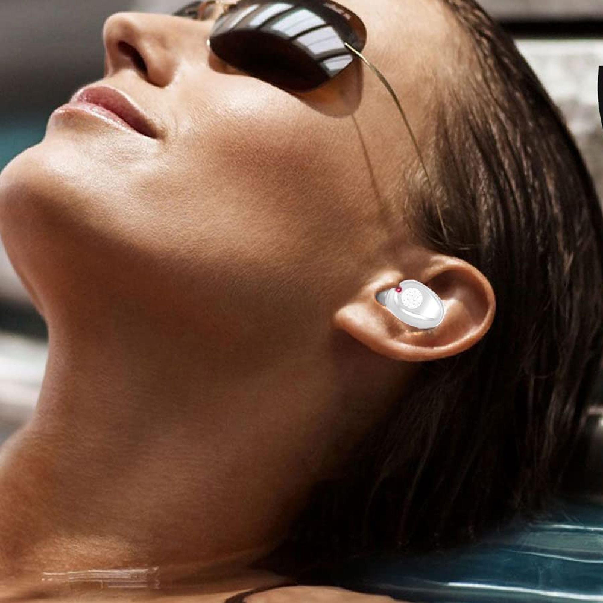 Eine Frau mit Sonnenbrille und Ohrstöpsel liegt im Wasser.