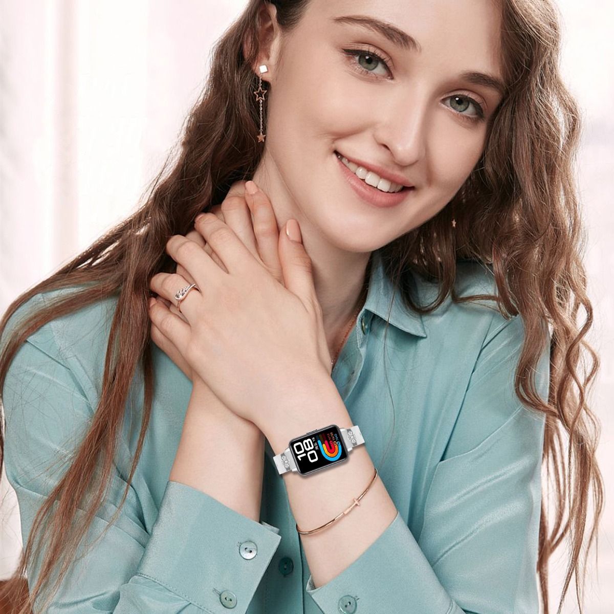 Frau mit blauem Hemd, verschränkten Händen, trägt eine weiße Smartwatch und ein Armband.