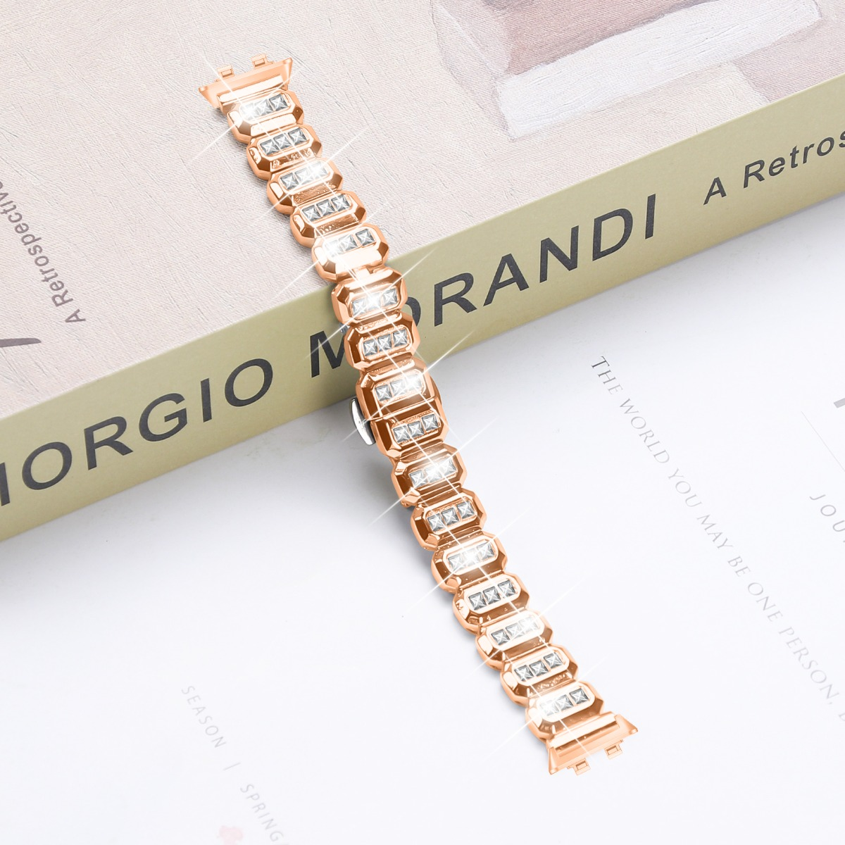 Un cinturino d'orologio color oro rosa con pietre rettangolari sfaccettate su un libro.