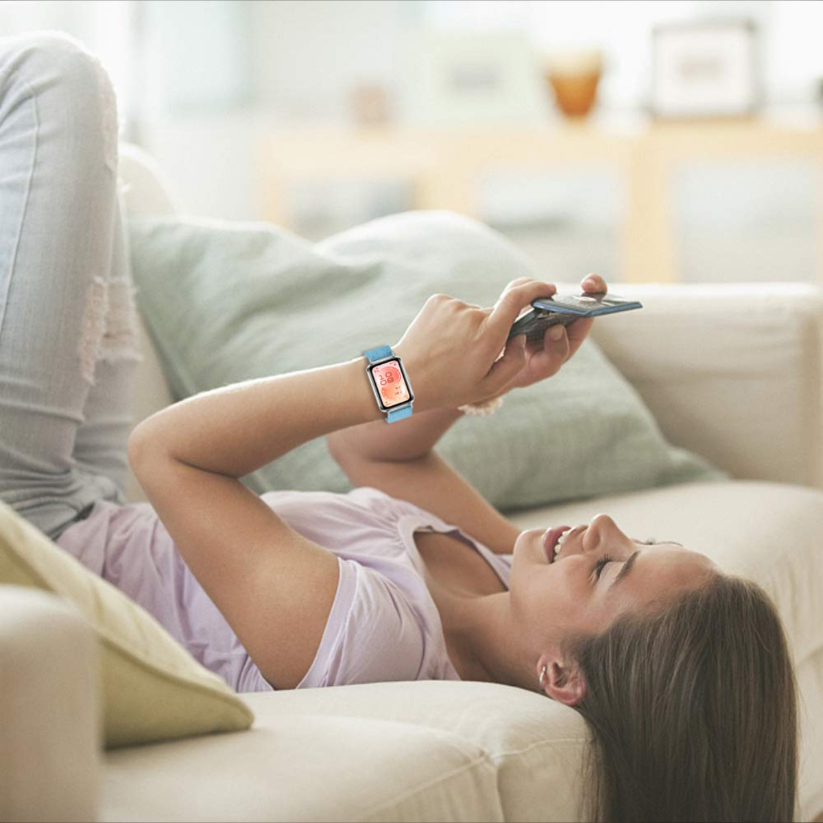 Una donna giace su un divano, guardando il suo telefono con uno smartwatch al polso.