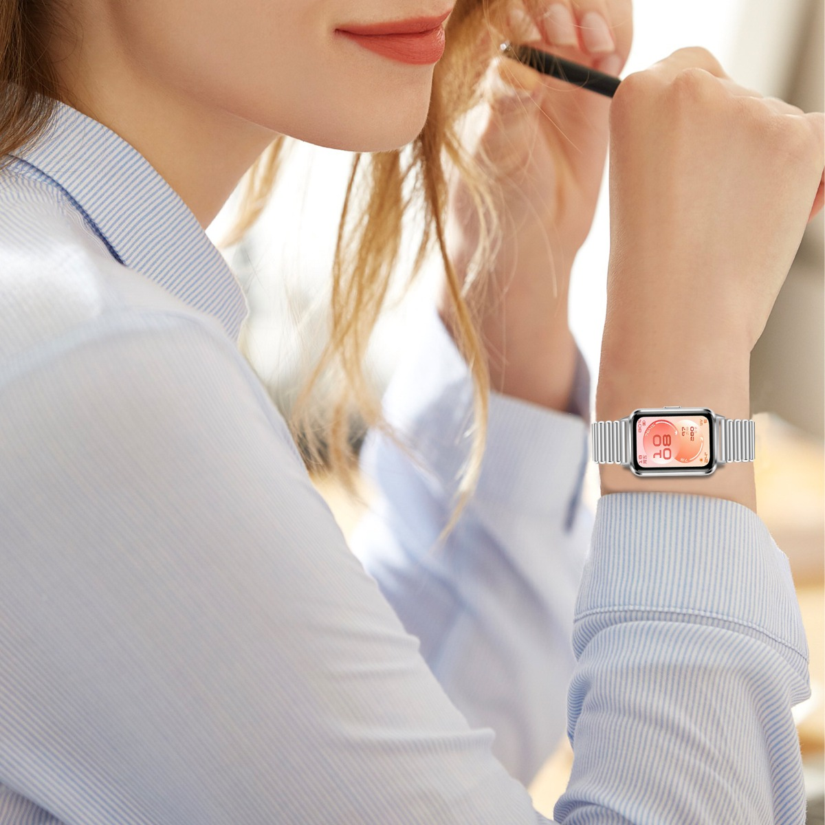 Eine Frau in einem blau gestreiften Hemd trägt eine silberne Smartwatch mit orangefarbenem Zifferblatt.