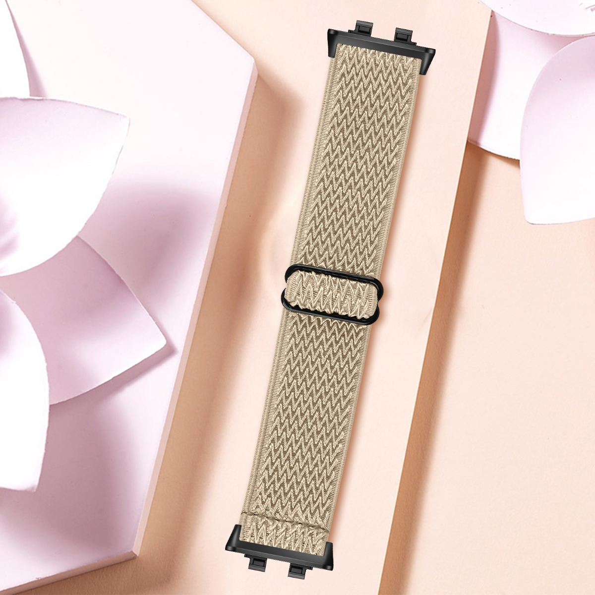Ein hellbeiges Stoffarmband mit Zickzackmuster und schwarzem Ring auf einem rosafarbenen Hintergrund.