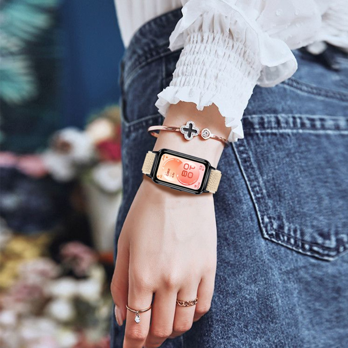 Eine Frau trägt eine Uhr mit hellem Band und ein Armband mit Kleeblattanhänger.