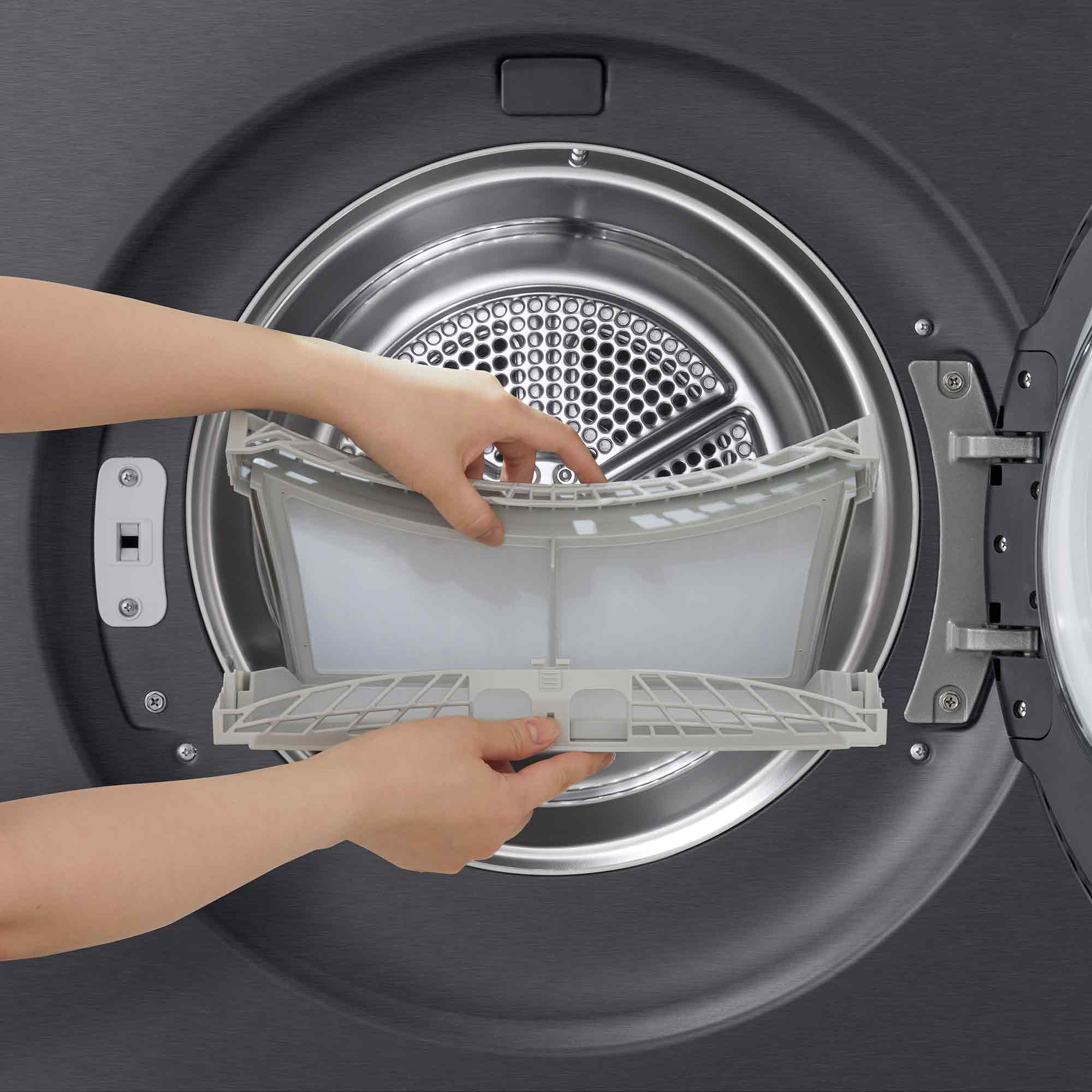 Hände entfernen einen grauen Flusenfilter aus einer dunklen Waschmaschine.