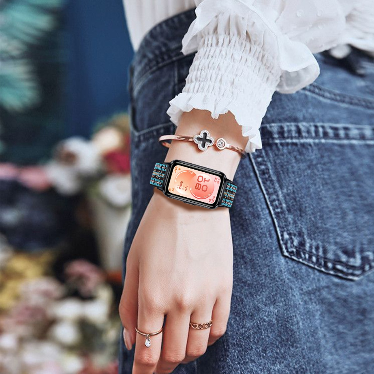 Eine Frau trägt eine Smartwatch mit blauem Armband und ein Armband mit Kleeblatt.