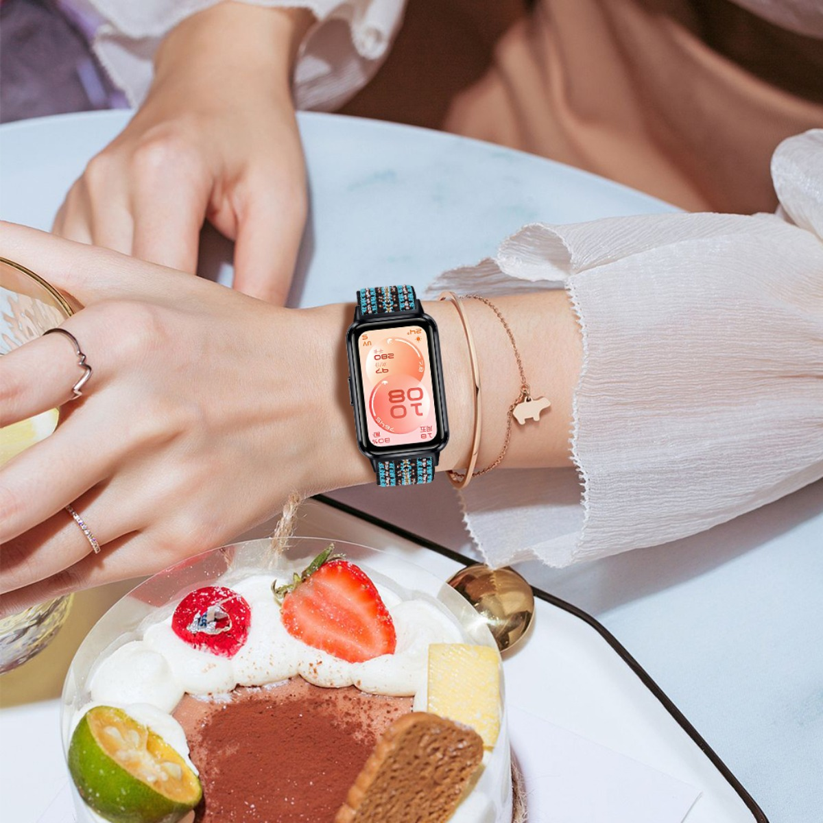 Eine Frau trägt eine Smartwatch mit blauem Band, neben einem Kuchen mit Früchten.