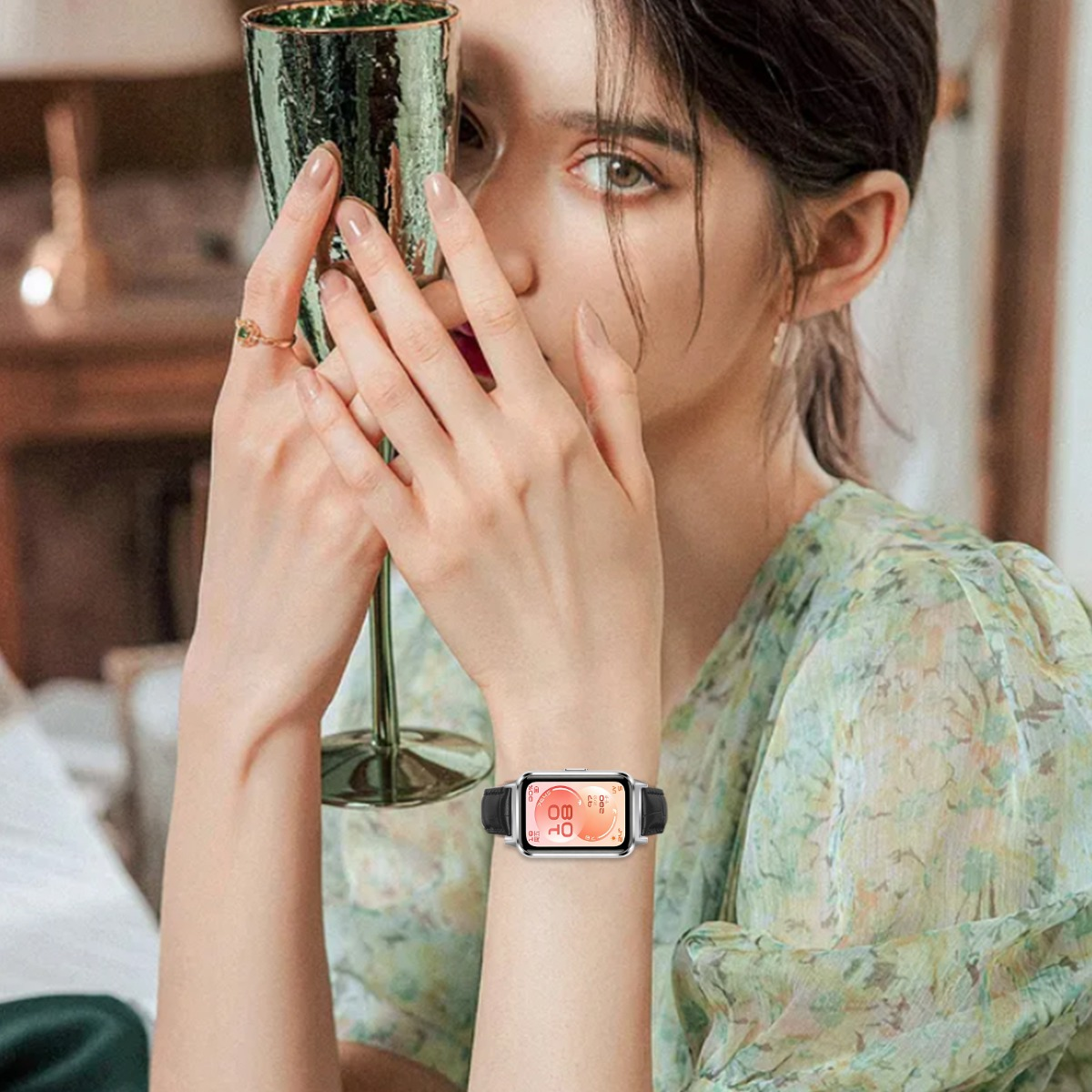 Eine Frau mit grünem Kleid hält ein Glas, trägt eine Smartwatch.