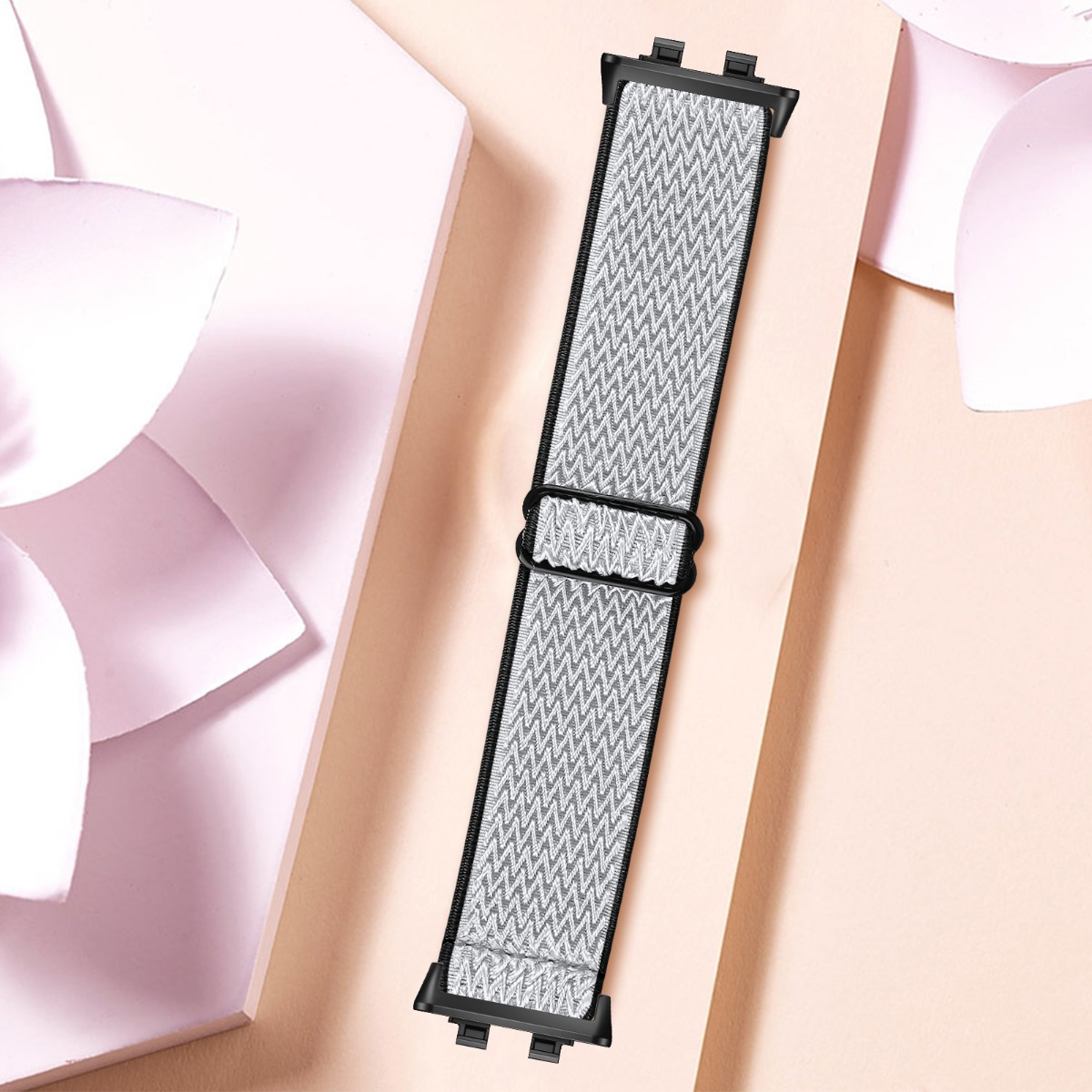 Cinturino per orologio in tessuto grigio con motivo a zigzag e connettori neri su sfondo rosa.