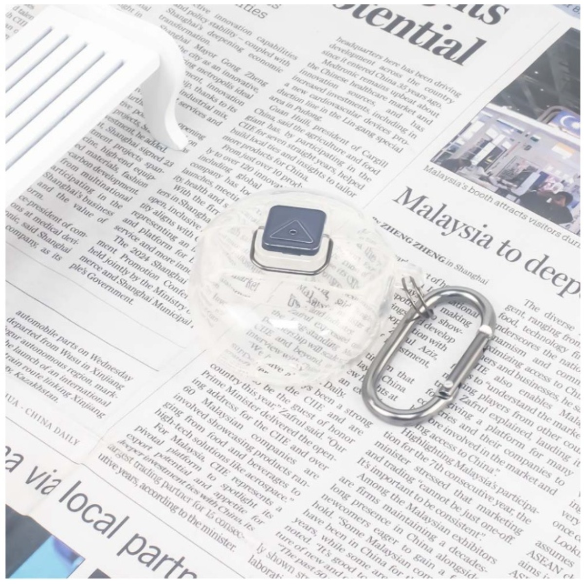 Un inserto in plastica trasparente con simbolo a triangolo blu giace su pagine di giornale.