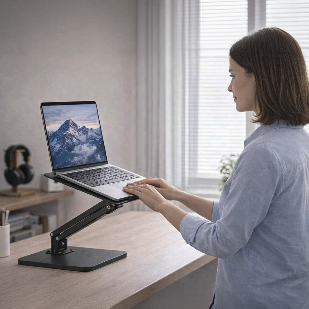 Eine Frau in einem blauen Hemd steht an einem Schreibtisch und benutzt einen Laptop auf einem Ständer.