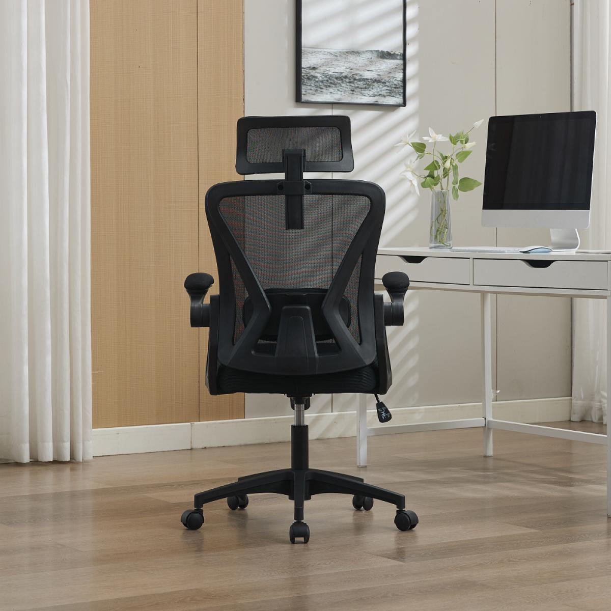 Ein schwarzer Bürostuhl mit Netzrücken und Kopfstütze steht vor einem Schreibtisch mit Computer.