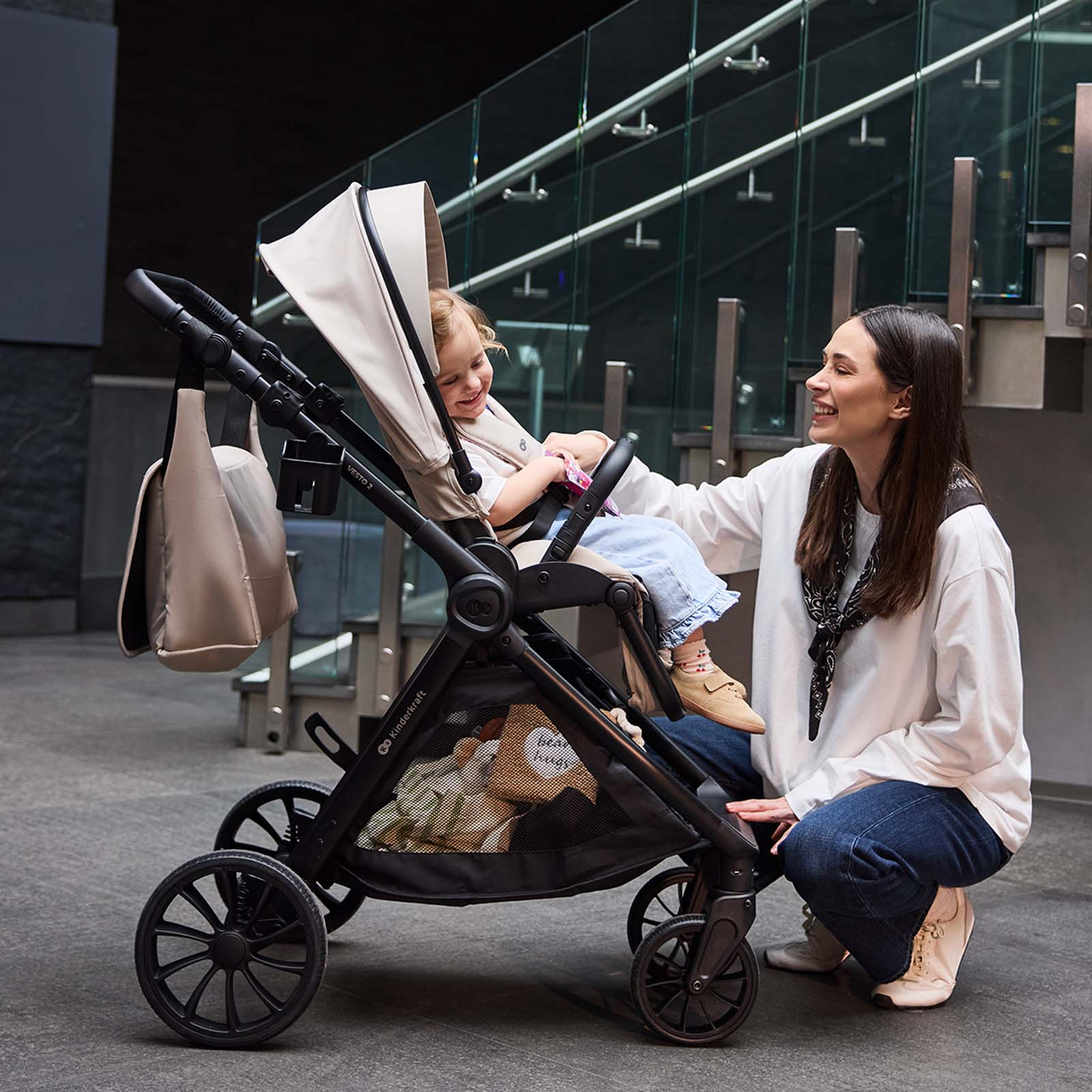 Eine Frau kniet neben einem Kinderwagen, in dem ein Kleinkind sitzt.