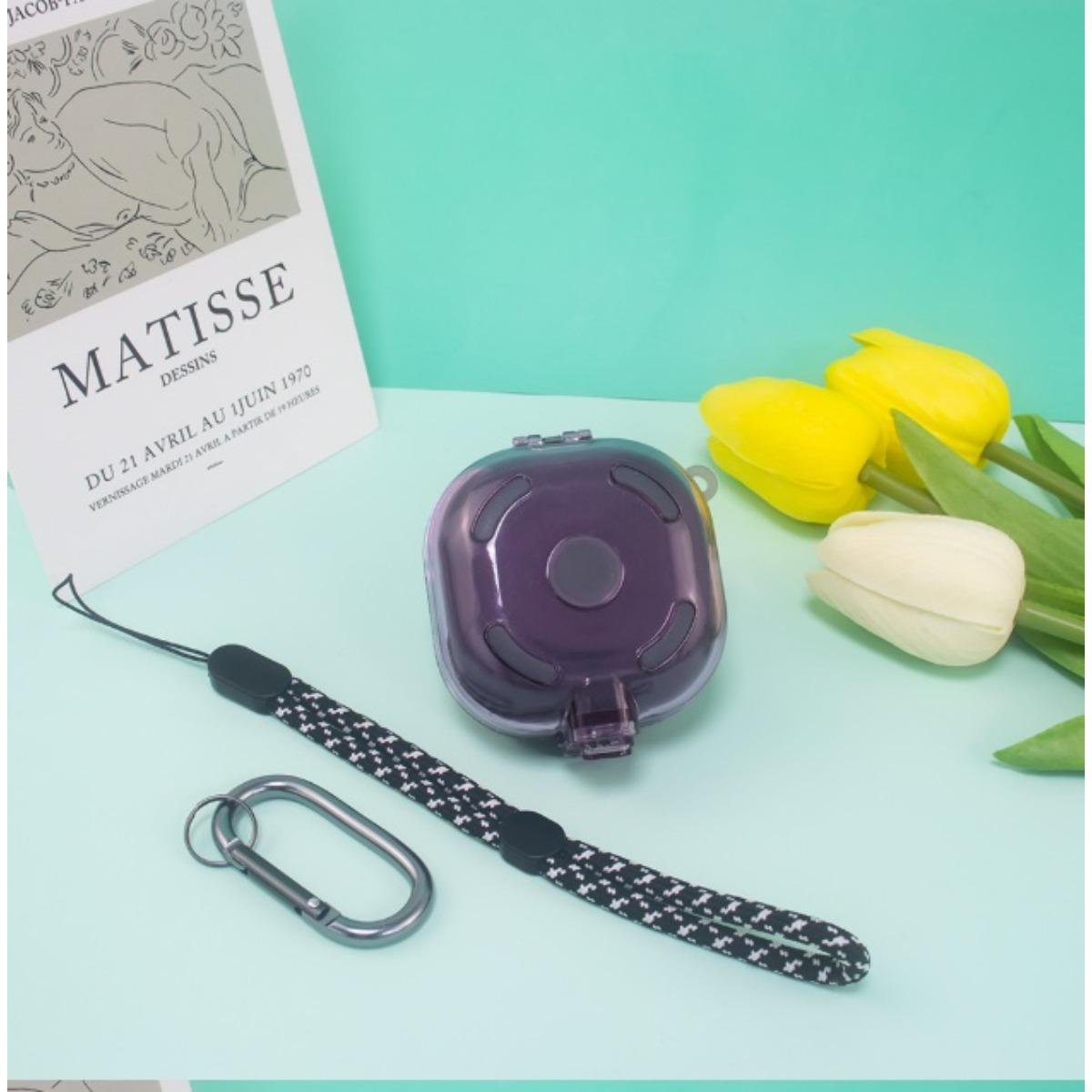 Lila Hülle mit Schlaufe und Karabinern neben Tulpen und Matisse-Poster.