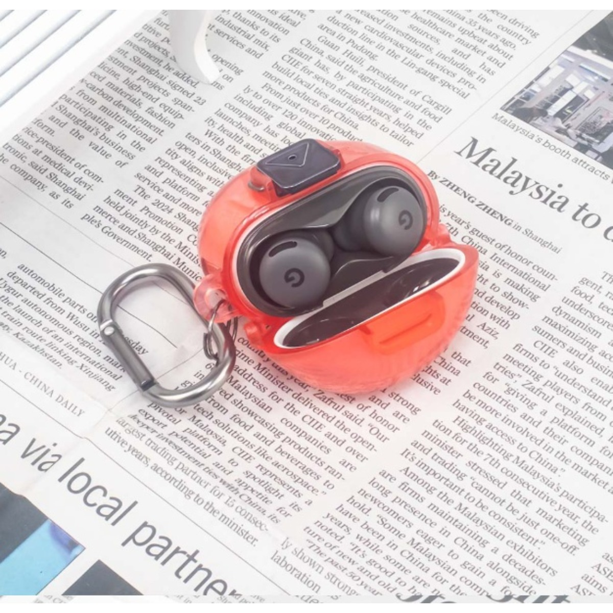 Rote Kopfhörer in einem transparenten Etui auf einer Zeitung.
