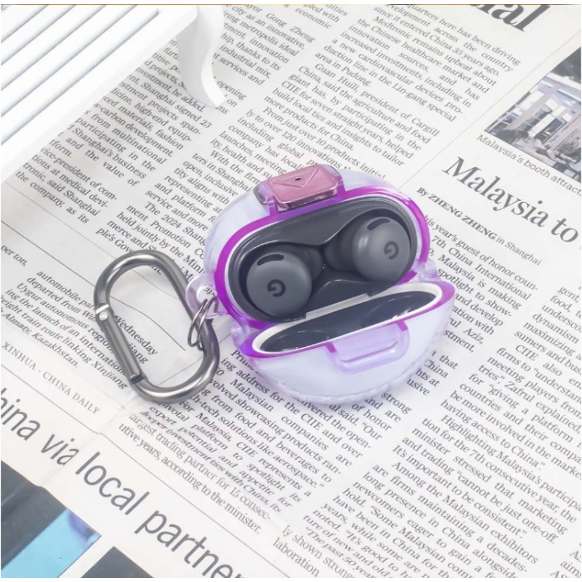 Una custodia trasparente per auricolari con accenti viola poggia su un giornale.