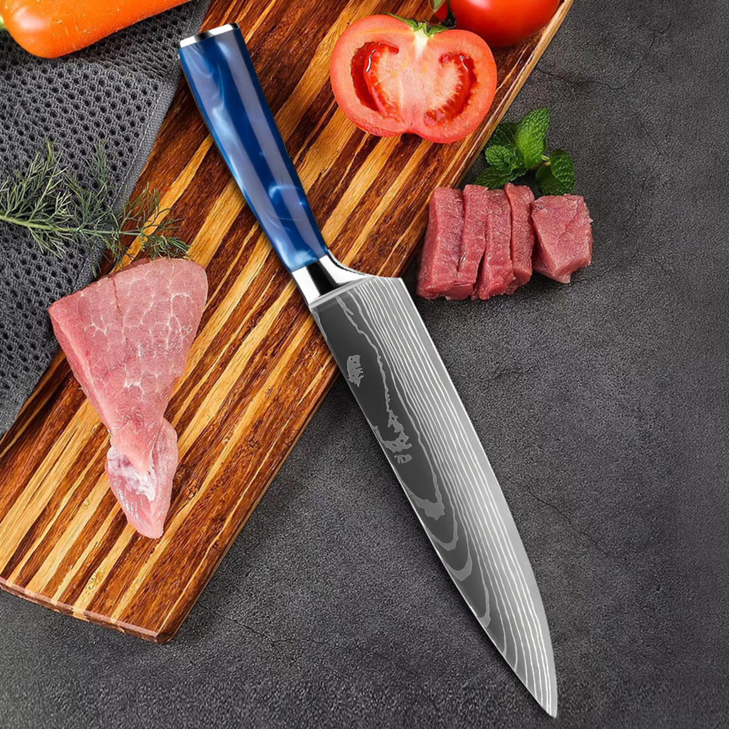 Un cuchillo de chef con mango azul descansa junto a carne, tomates y hierbas en una tabla de cortar.