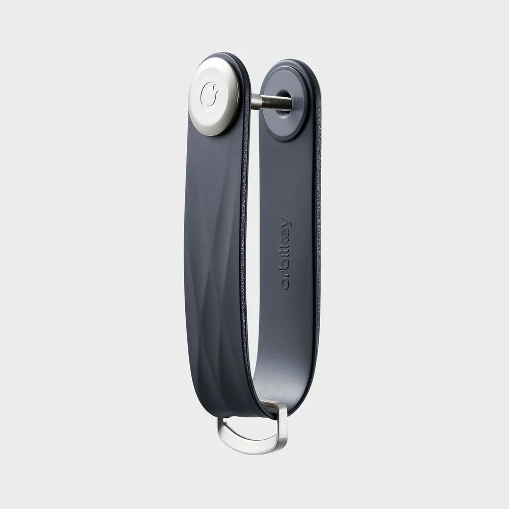 Un organizer per chiavi Orbitkey scuro con accenti argentati su sfondo grigio.