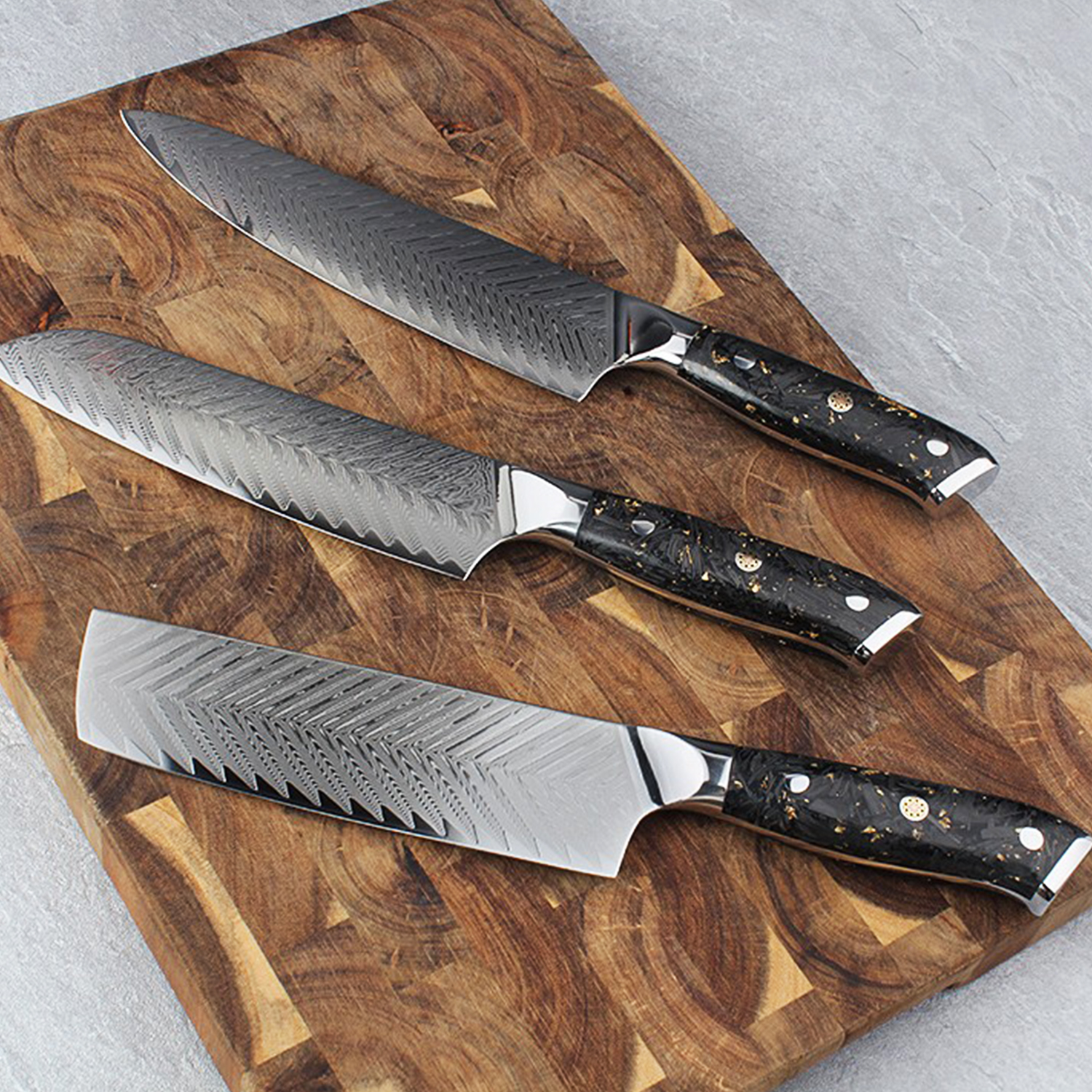 Tres cuchillos de cocina Damasco con mangos negros sobre tabla de cortar.