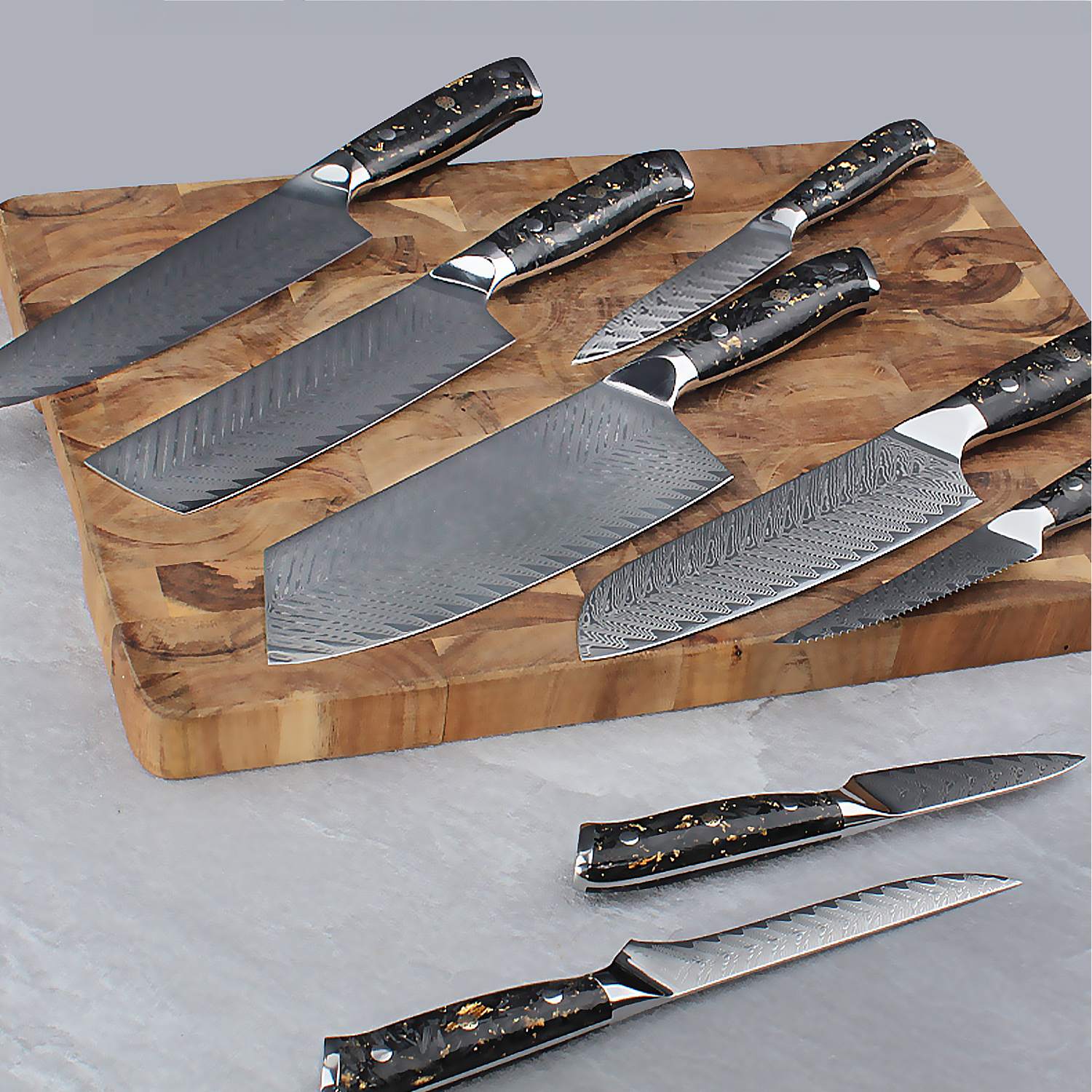Una colección de cuchillos de acero Damasco con mangos negros y dorados en una tabla de madera.
