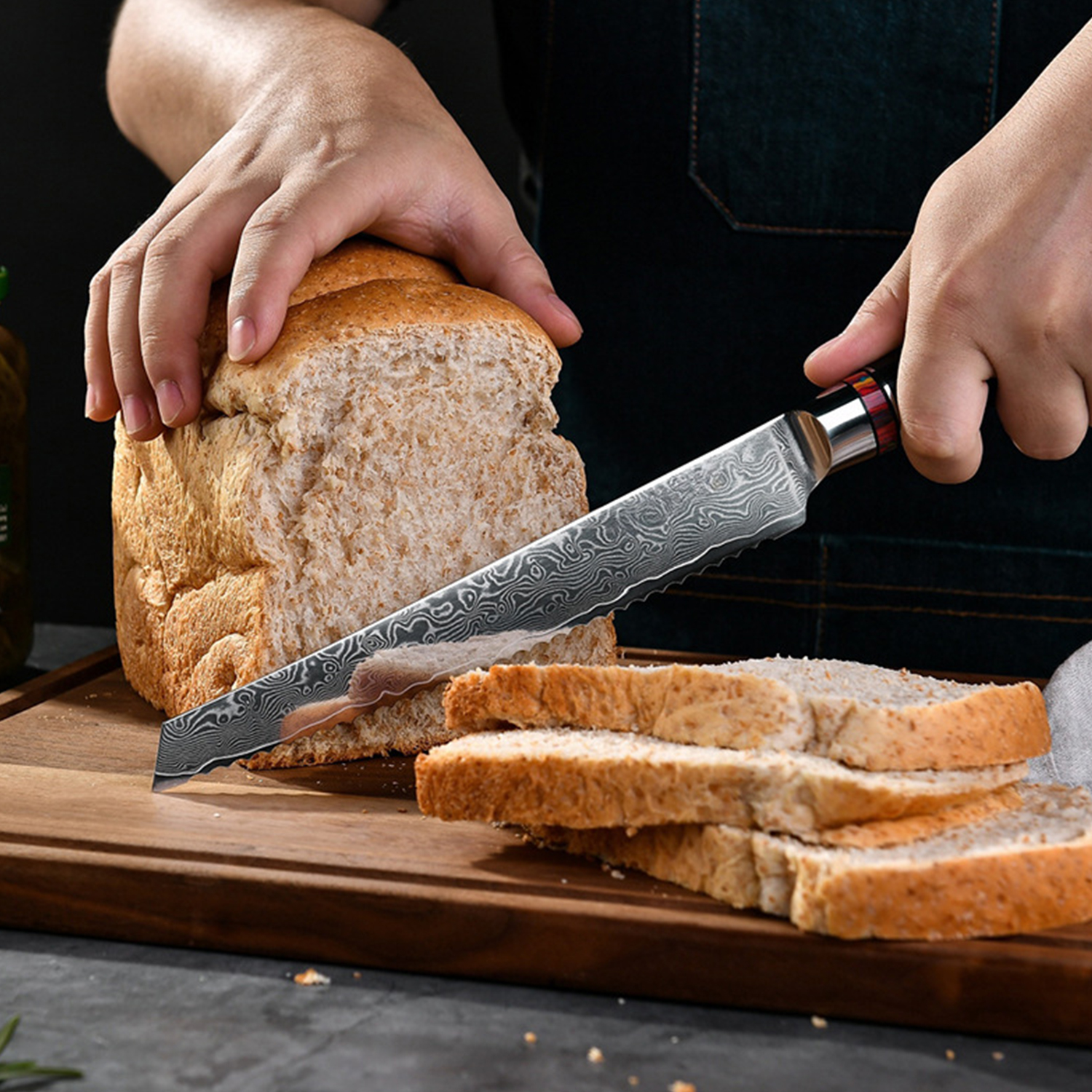 Manos cortando un pan con cuchillo damasquino sobre tabla de madera.
