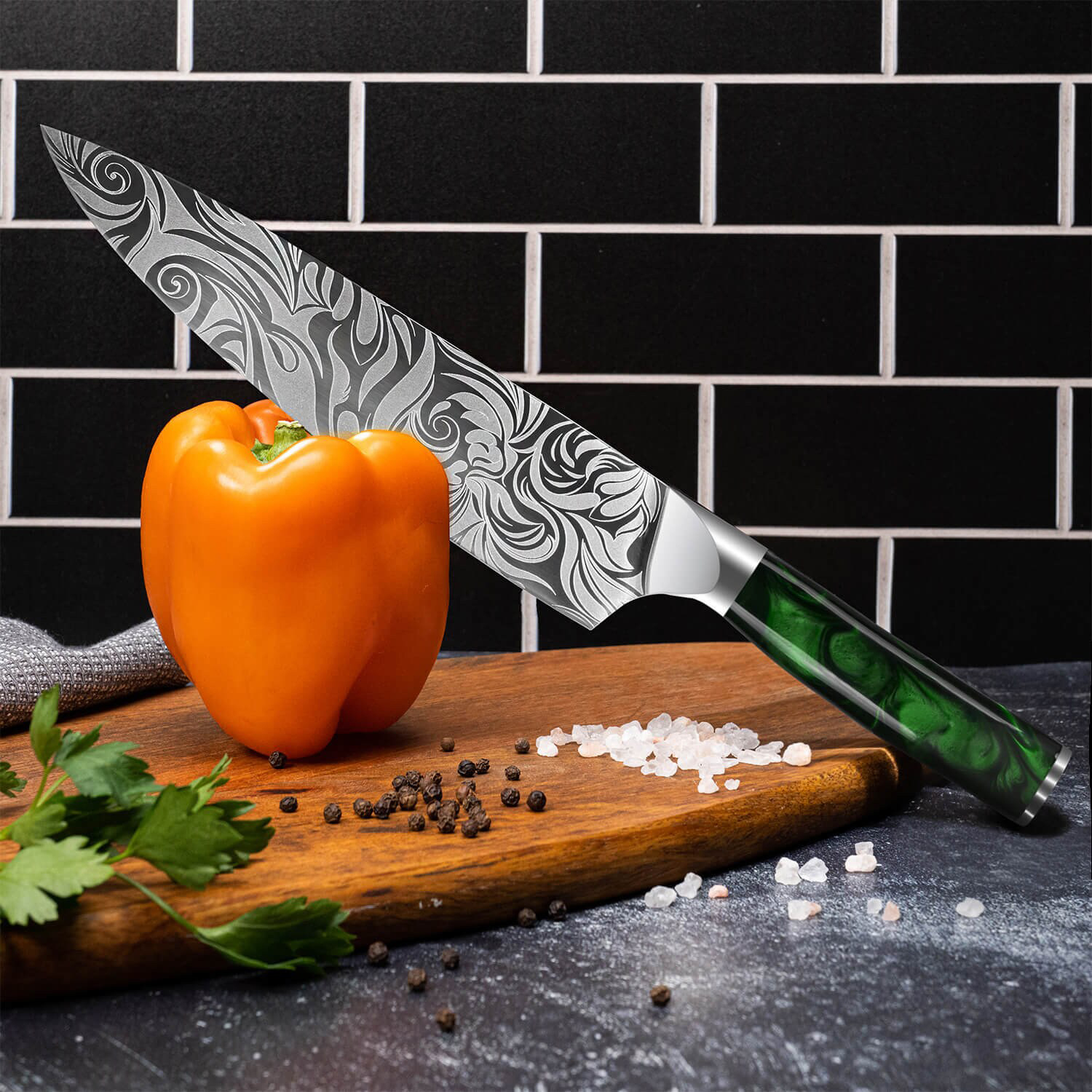 Un cuchillo de chef con hoja estampada descansa sobre una tabla de cortar junto a un pimiento naranja.