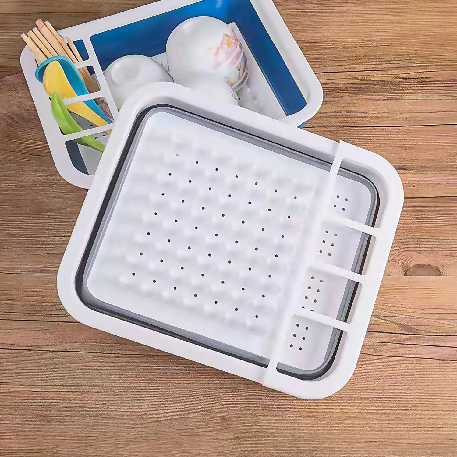 Un escurreplatos plegable blanco con inserto azul y utensilios.