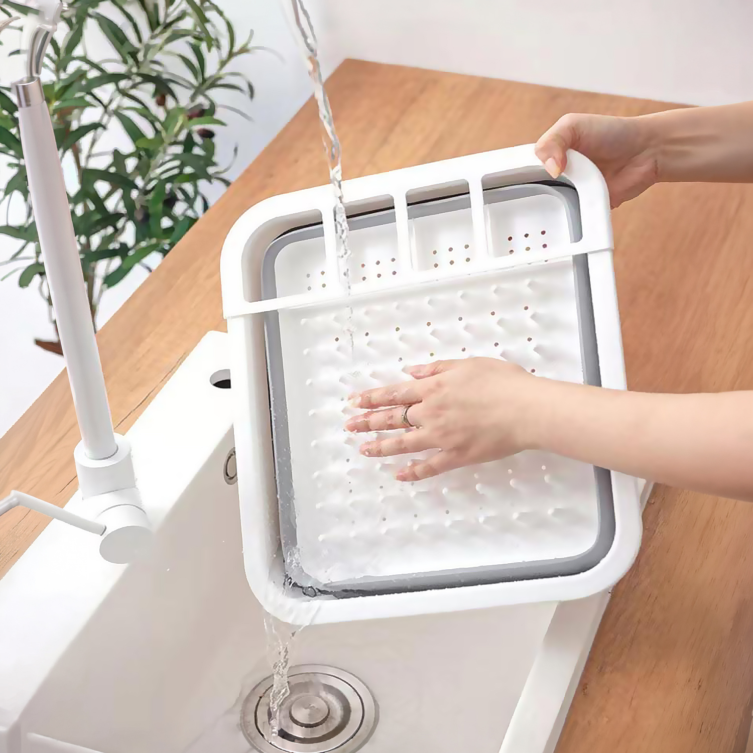 El agua cae en una cesta de fregadero plegable blanca sostenida por manos sobre un fregadero de cocina.
