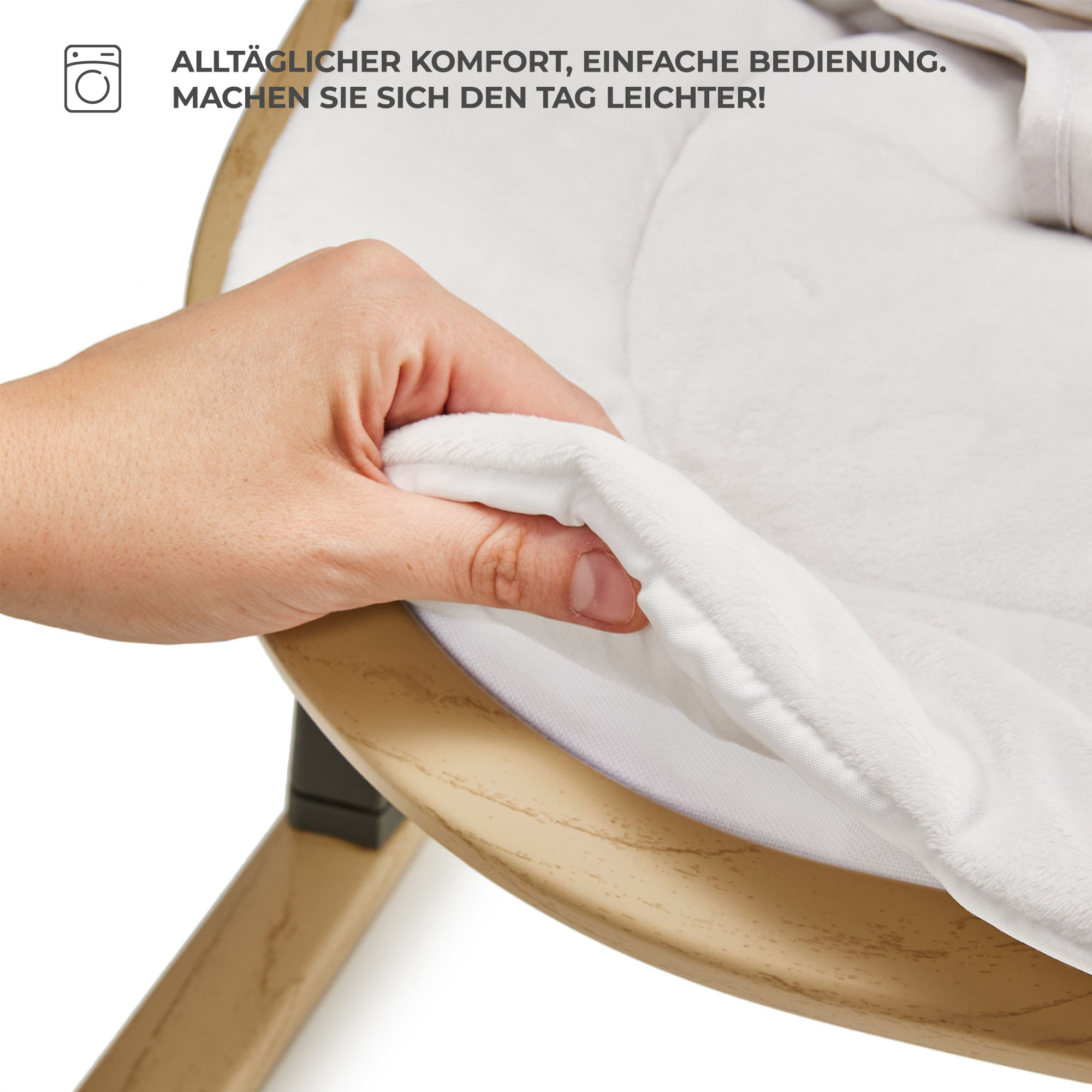 Hand berührt weichen, weißen Stoff eines Babybettes. Waschsymbol oben links.