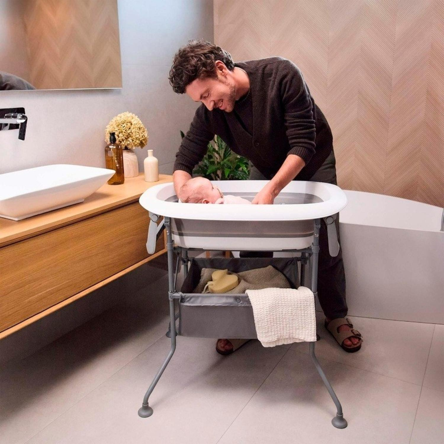 Ein Mann wäscht ein Baby in einer Babybadewanne in einem Badezimmer.