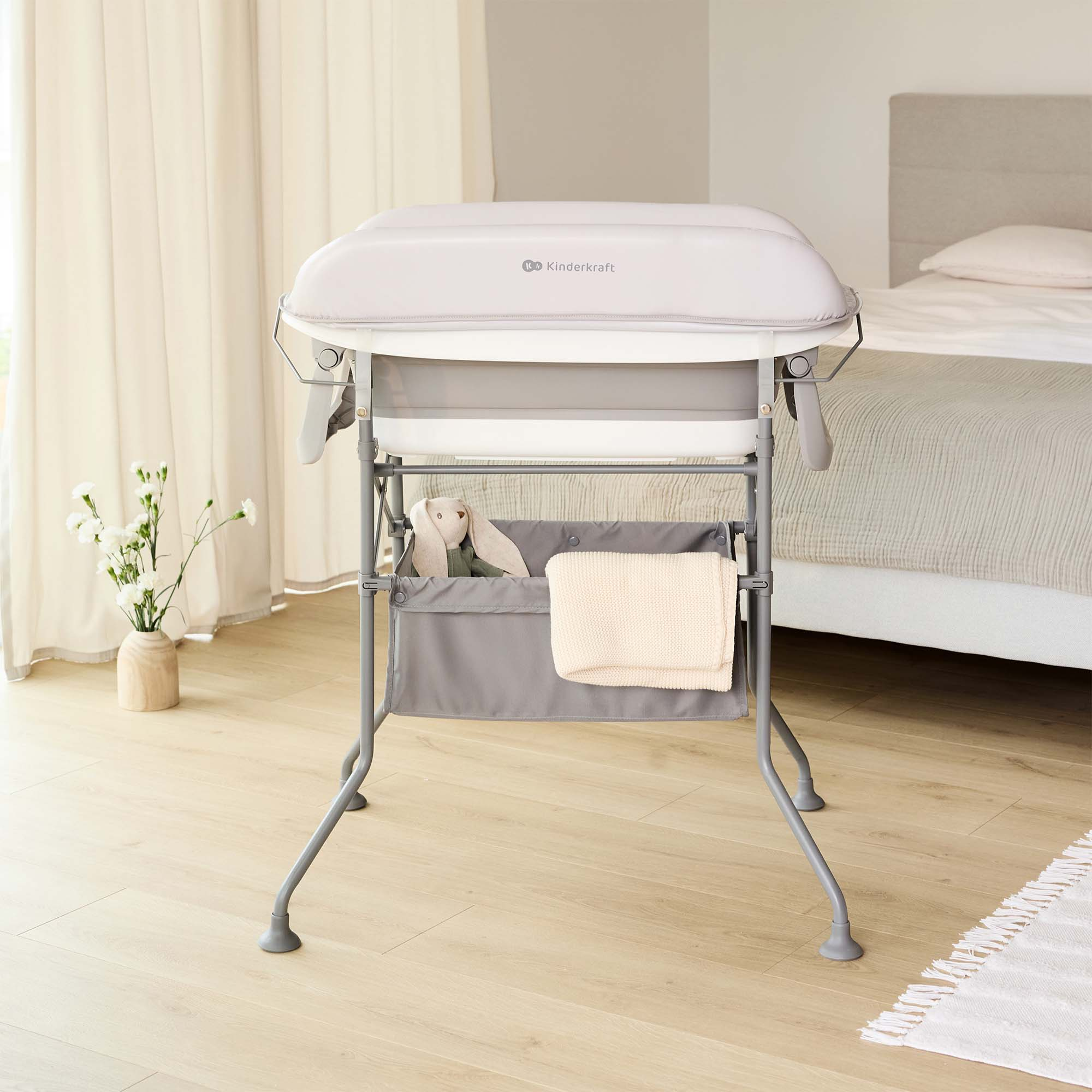 Ein Babywickeltisch mit Aufbewahrungstasche und Spielzeug, neben einem Bett.