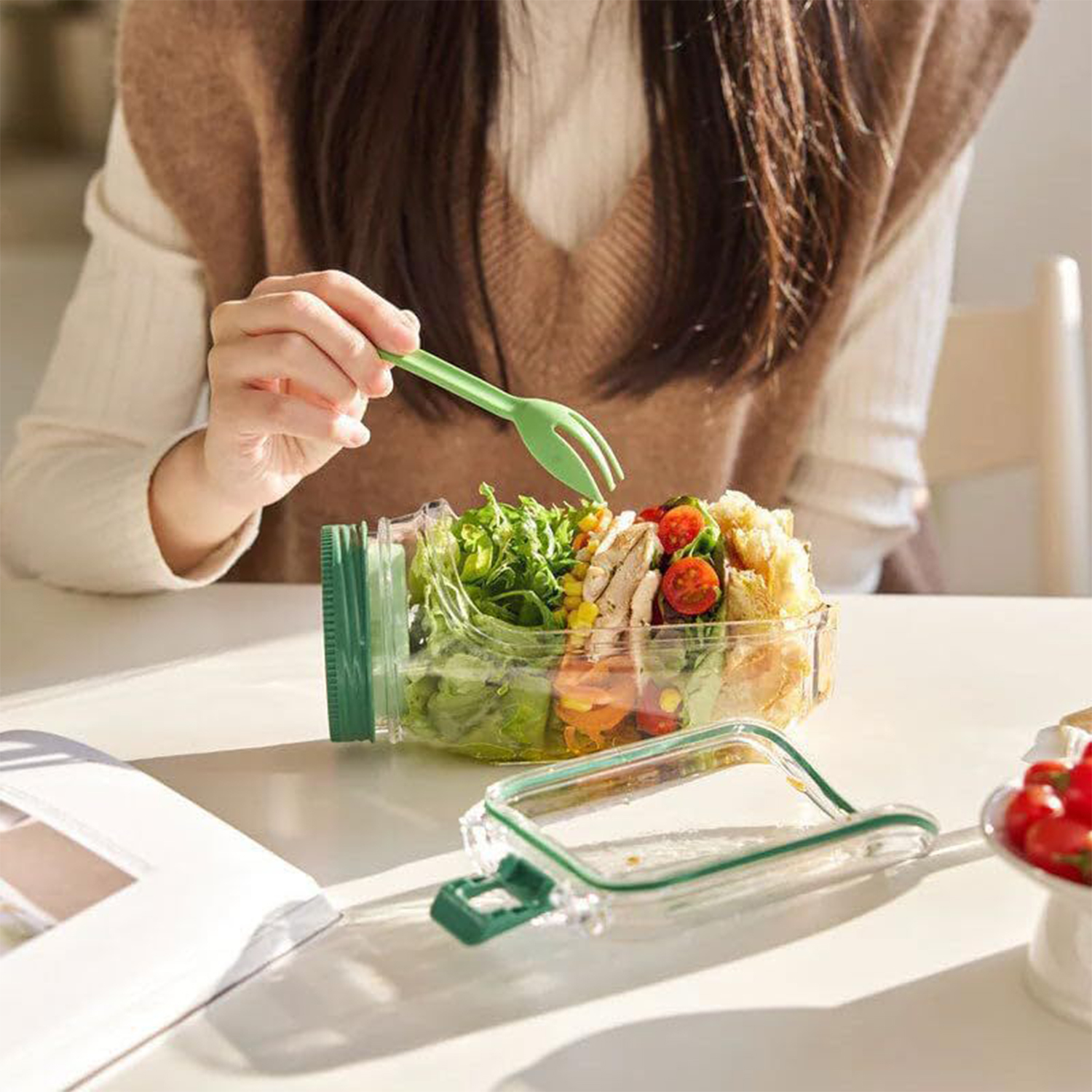 Una persona comiendo una ensalada de un recipiente de vidrio con un tenedor verde.