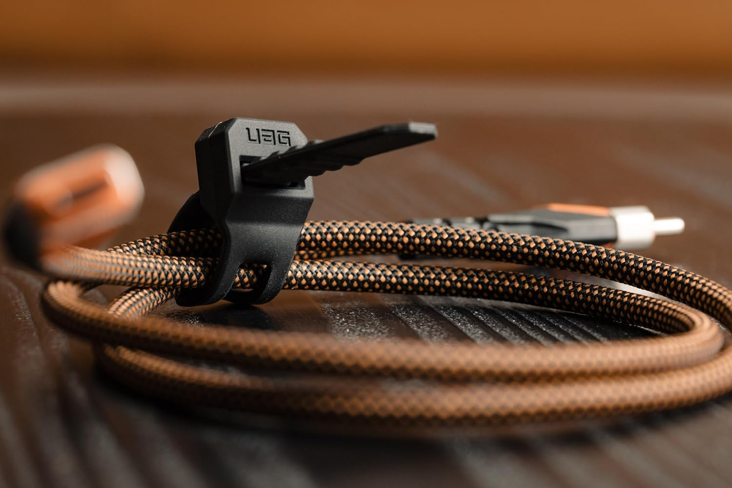 Czarno-pomarańczowy kabel z czarnym klipsem UAG na drewnianym stole.