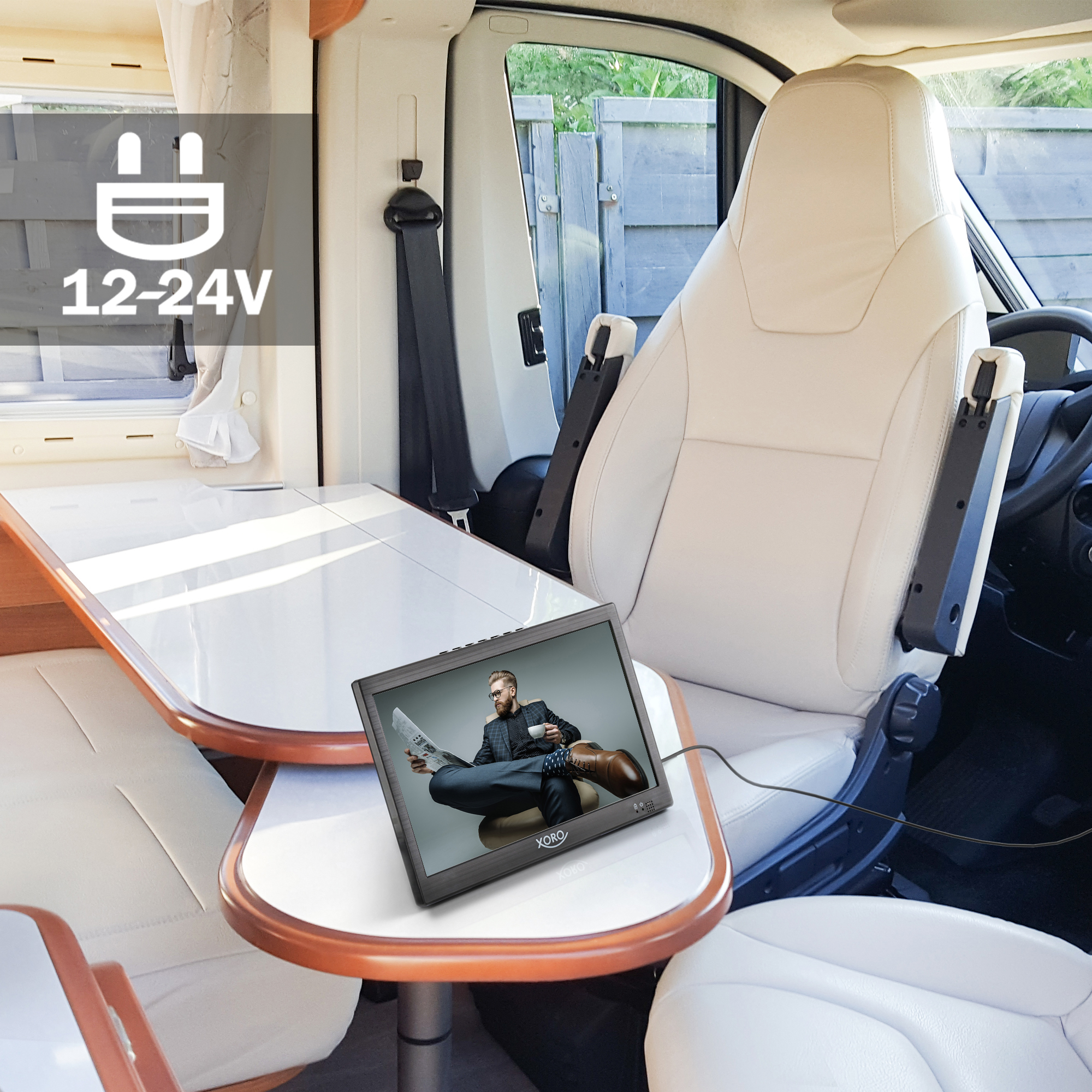 Vista interior de una autocaravana con mesa y monitor que muestra a un hombre.