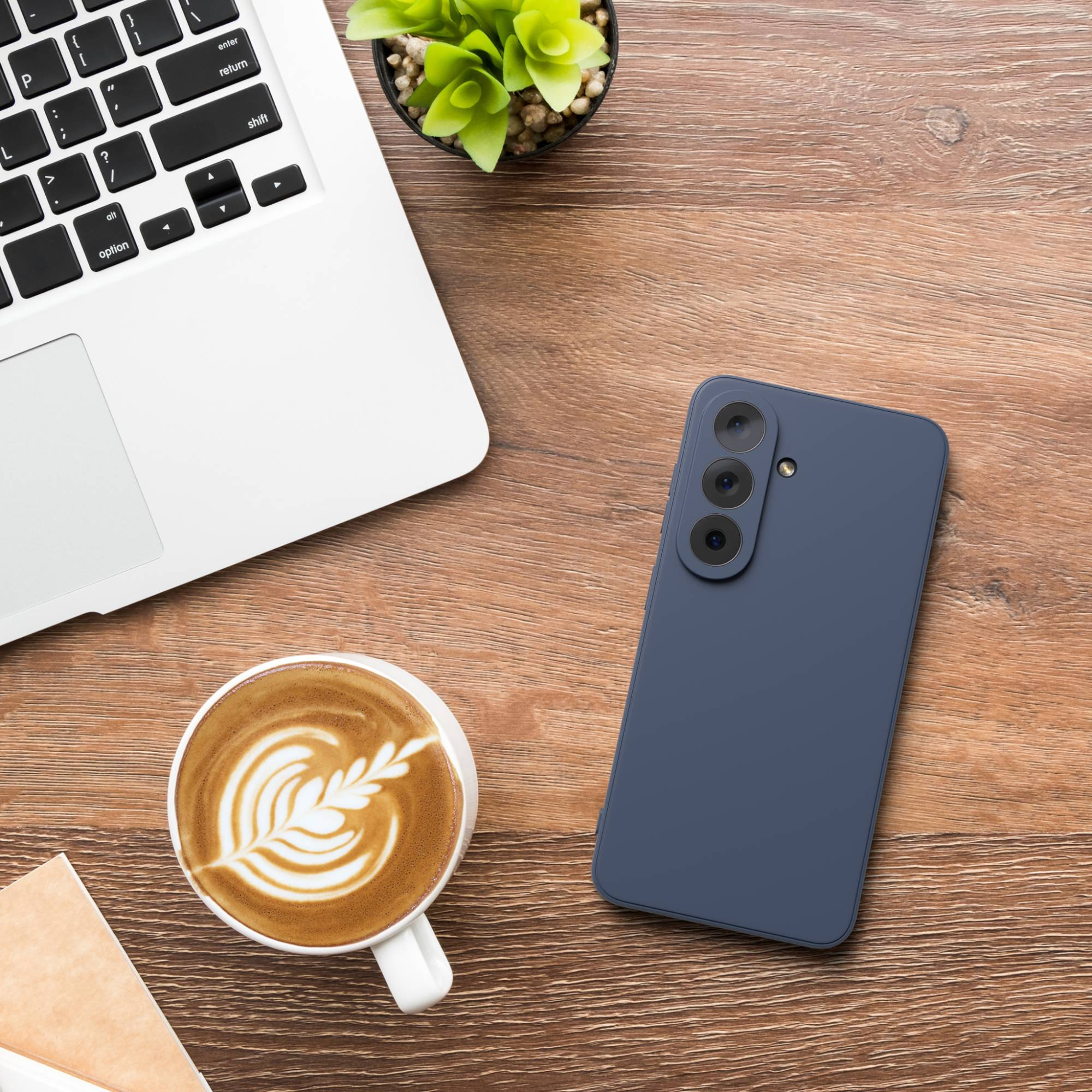 Ein Laptop, eine Kaffeetasse mit Latte Art und ein Smartphone auf einem Holztisch.
