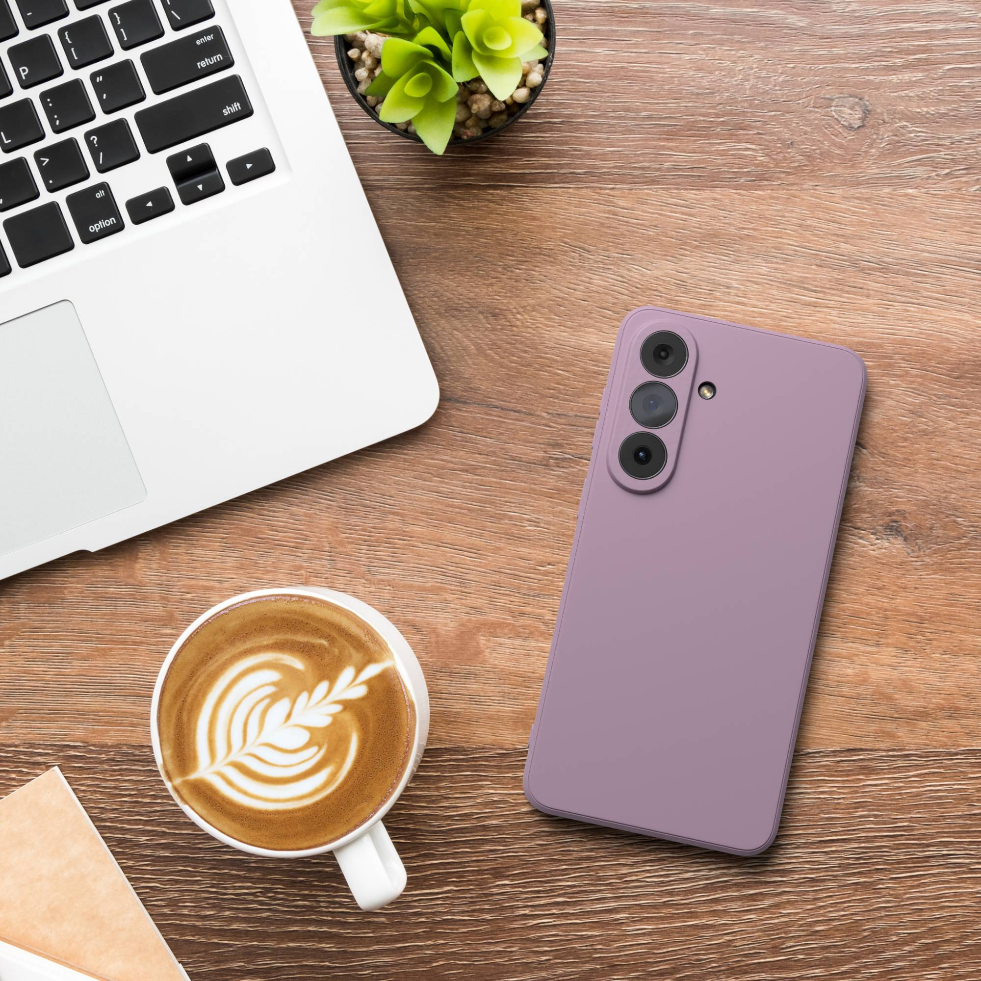 Ein violettes Smartphone mit drei Kameras liegt auf einem Holztisch neben einem Laptop und Kaffee.