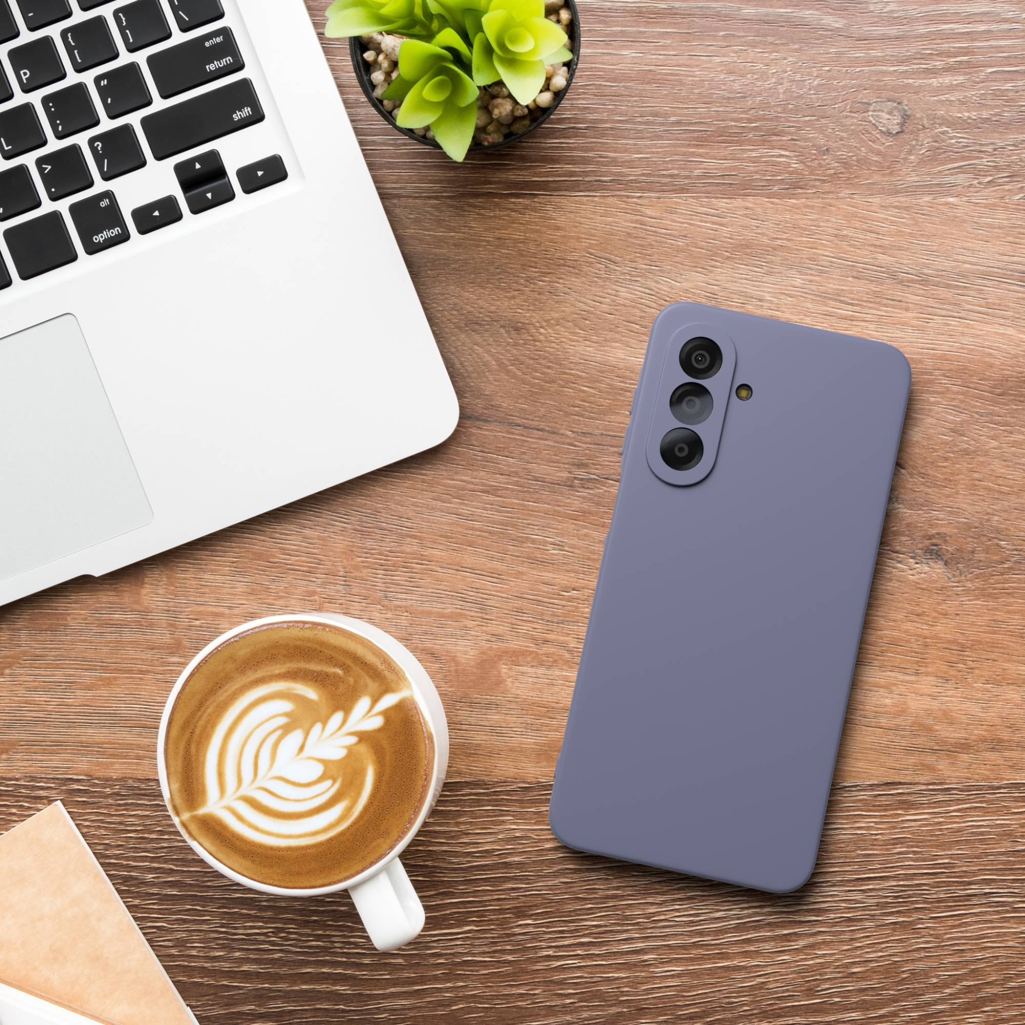 Ein Laptop, eine Kaffeetasse mit Latte Art und ein violettes Handy auf einem Holztisch.