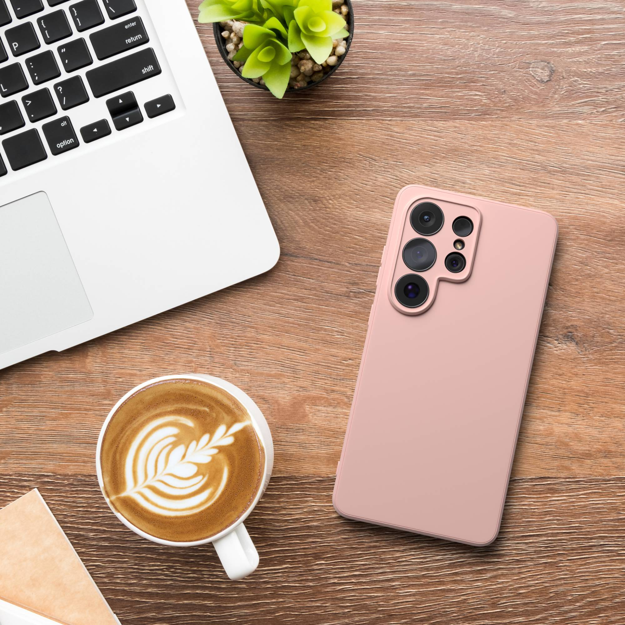 Ein rosafarbener Handy, ein Laptop, eine Kaffeetasse und eine Pflanze auf einem Holztisch.