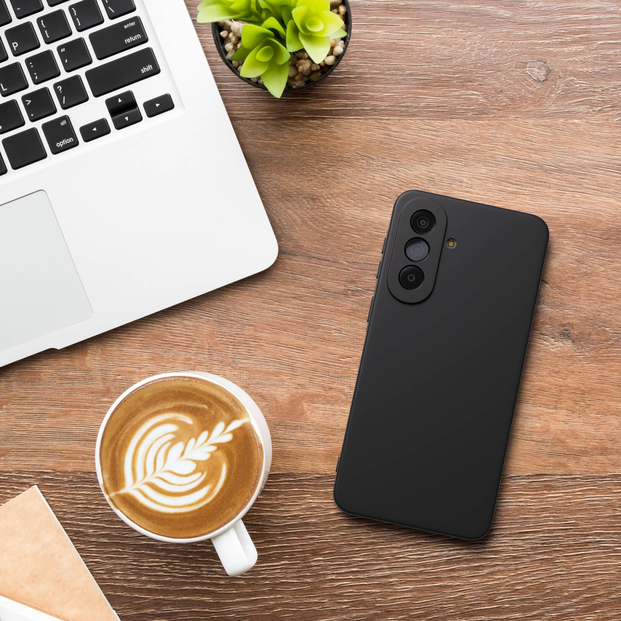 Ein schwarzes Smartphone, eine weiße Tasse mit Latte Art und ein Laptop liegen auf einem Holztisch.