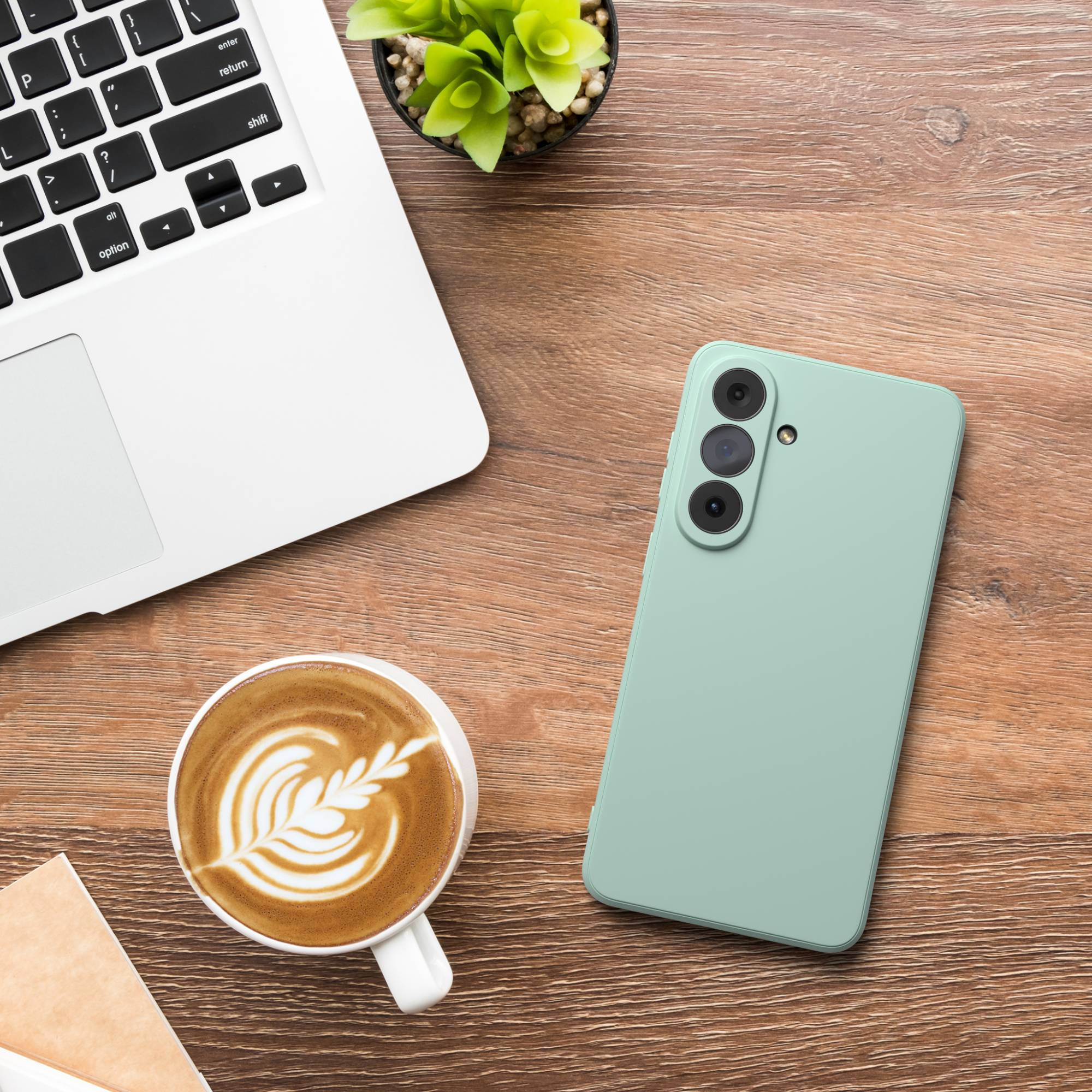 Ein Laptop, eine Kaffeetasse mit Latte Art, ein Handy und eine Pflanze auf einem Holztisch.